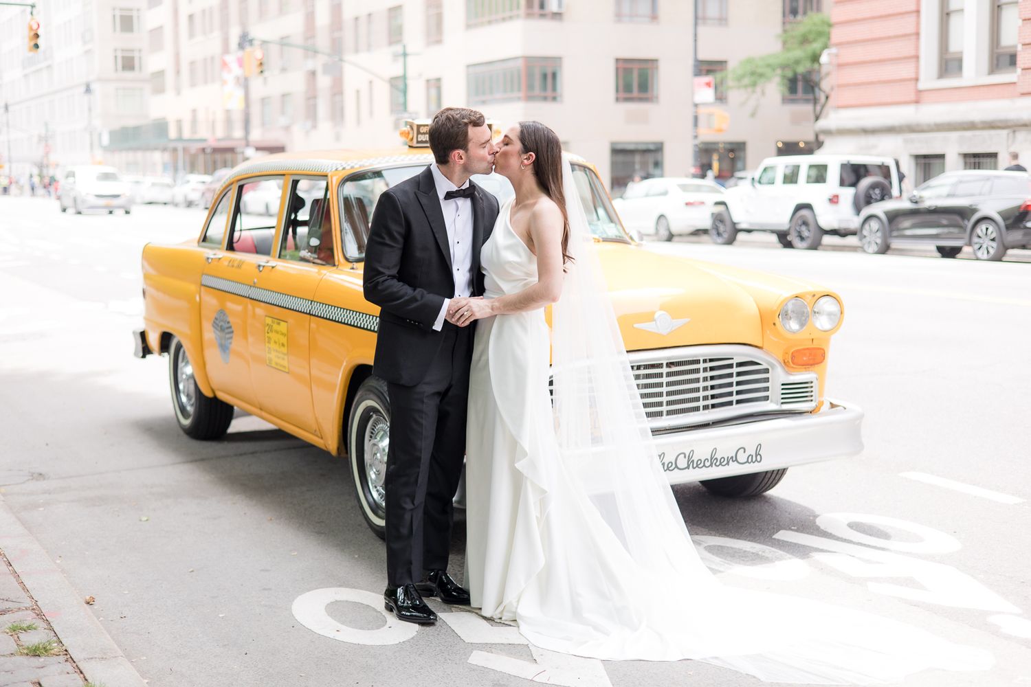 Newlyweds pose alongside a classic yellow taxi cab on a Manhattan street.