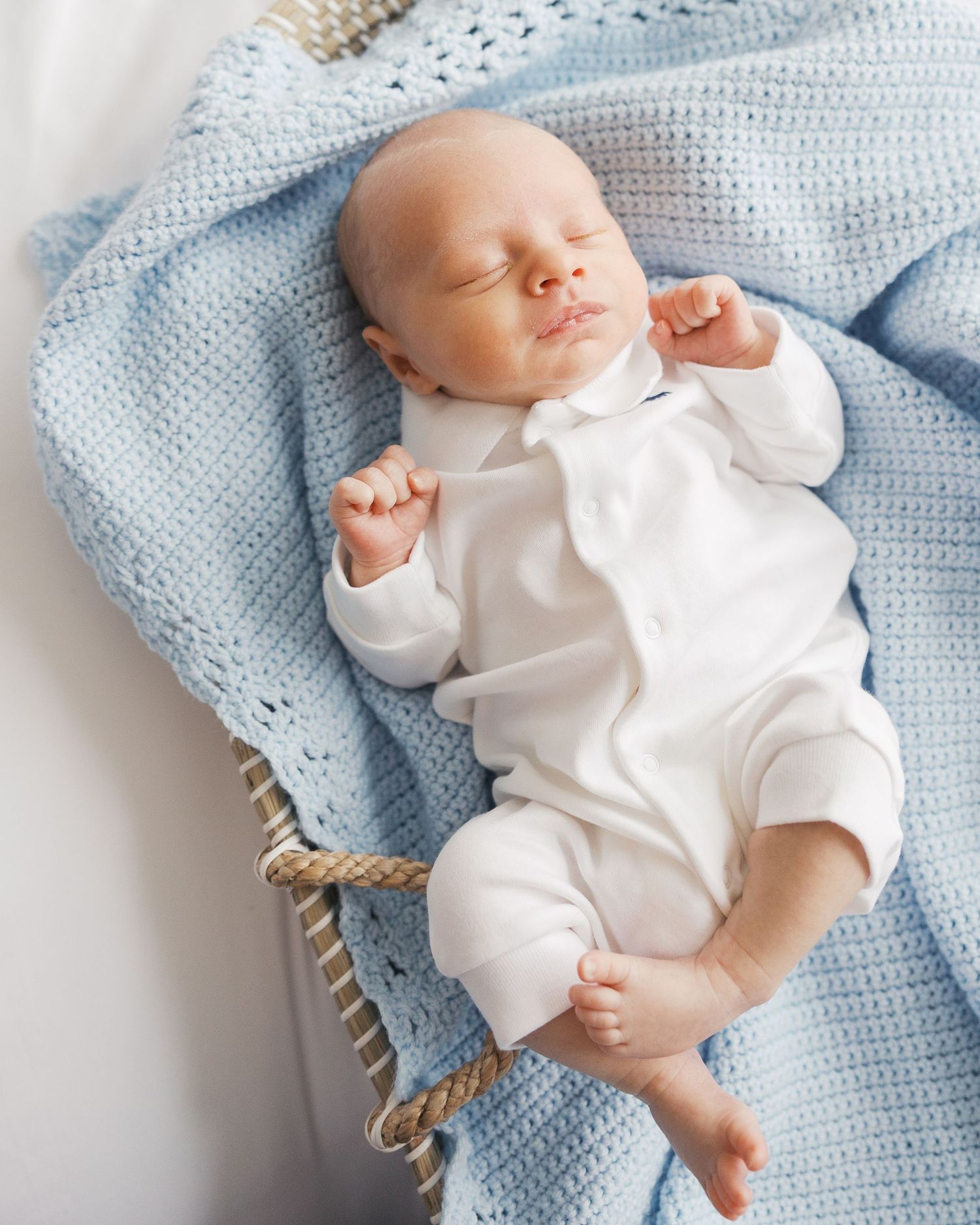 A sleeping newborn in white clothing rests peacefully on a soft blue knit blanket.