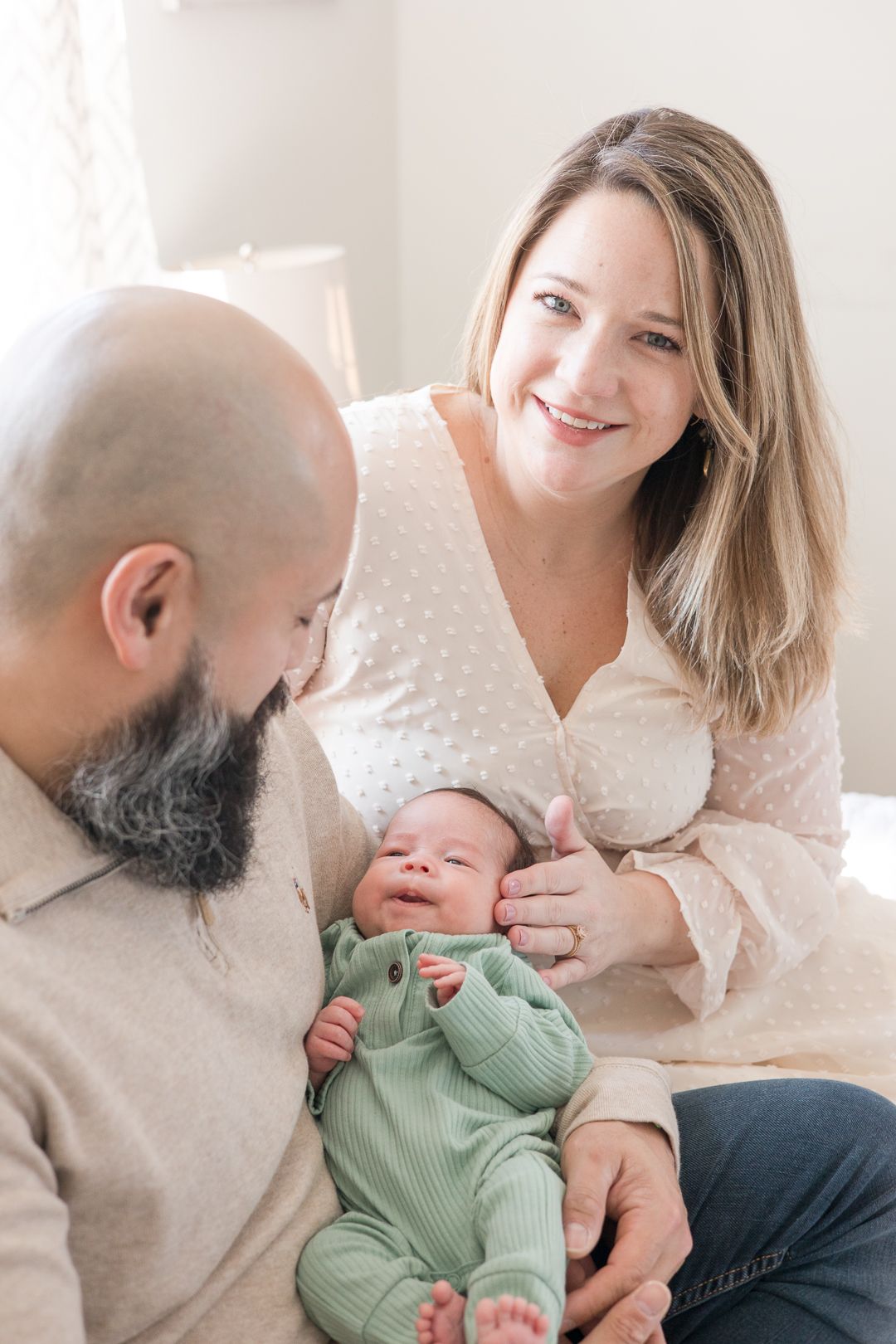 An intimate family portrait with a baby in mint green against a bright white background.