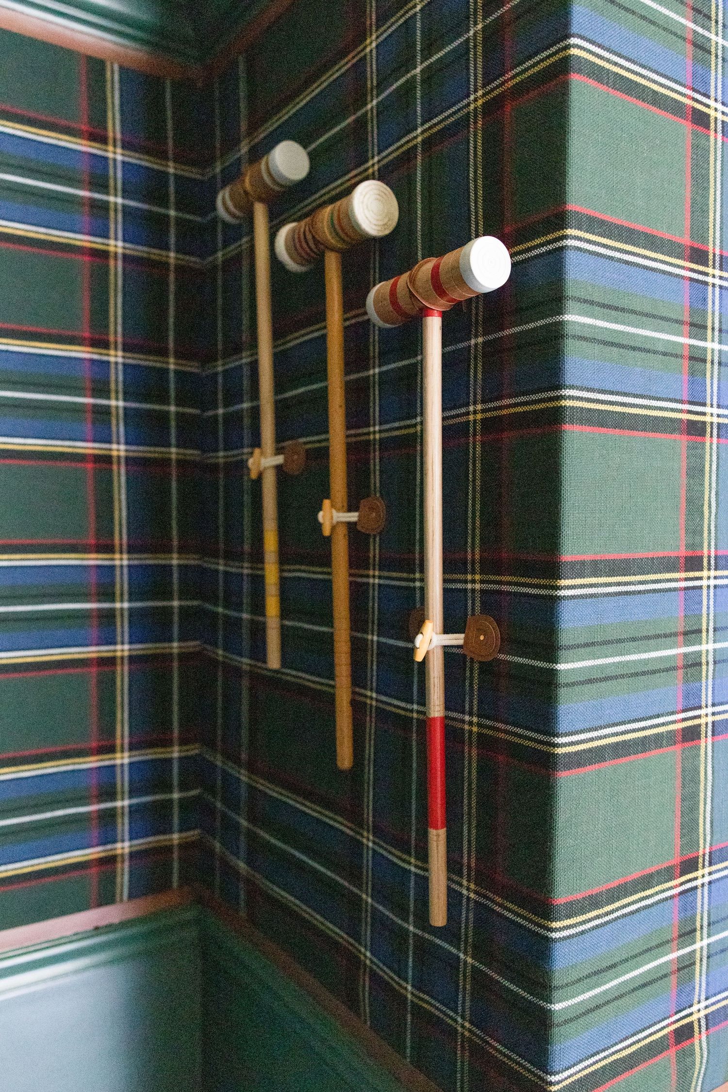 Croquet mallets mounted on dark green plaid wallpapered walls.