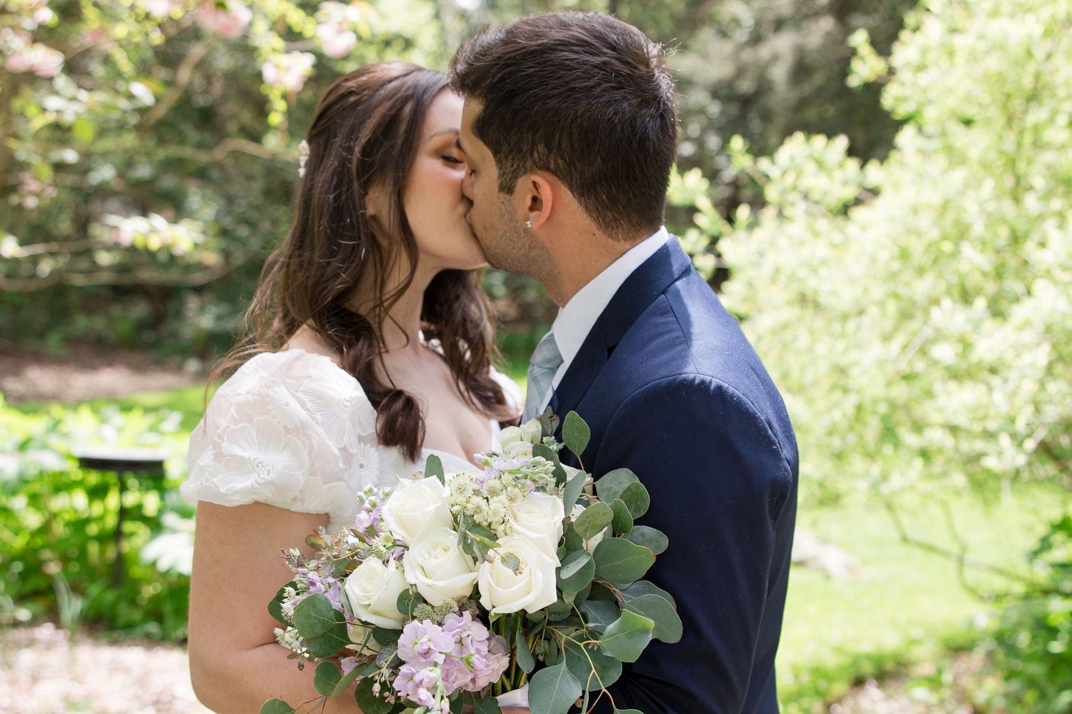 A romantic wedding moment captured as a couple shares a kiss surrounded by blooming spring gardens.