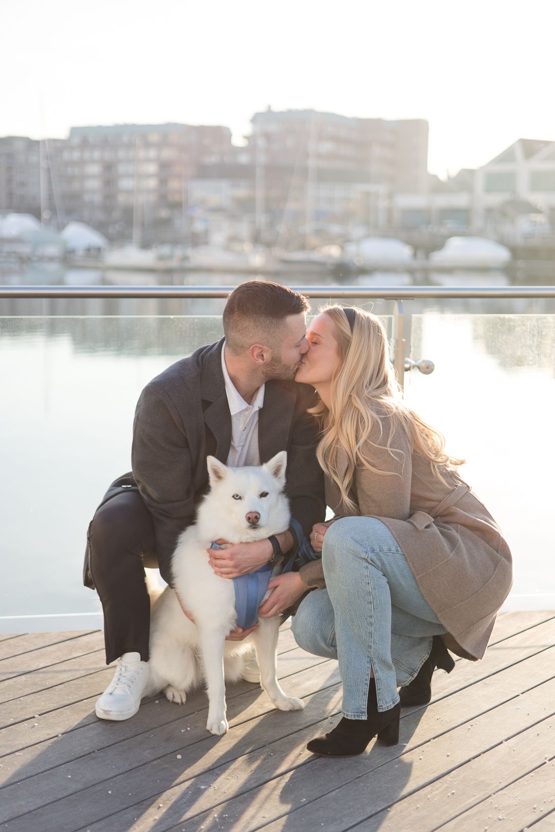 A couple shares an intimate moment with their white Husky dog by the waterfront.