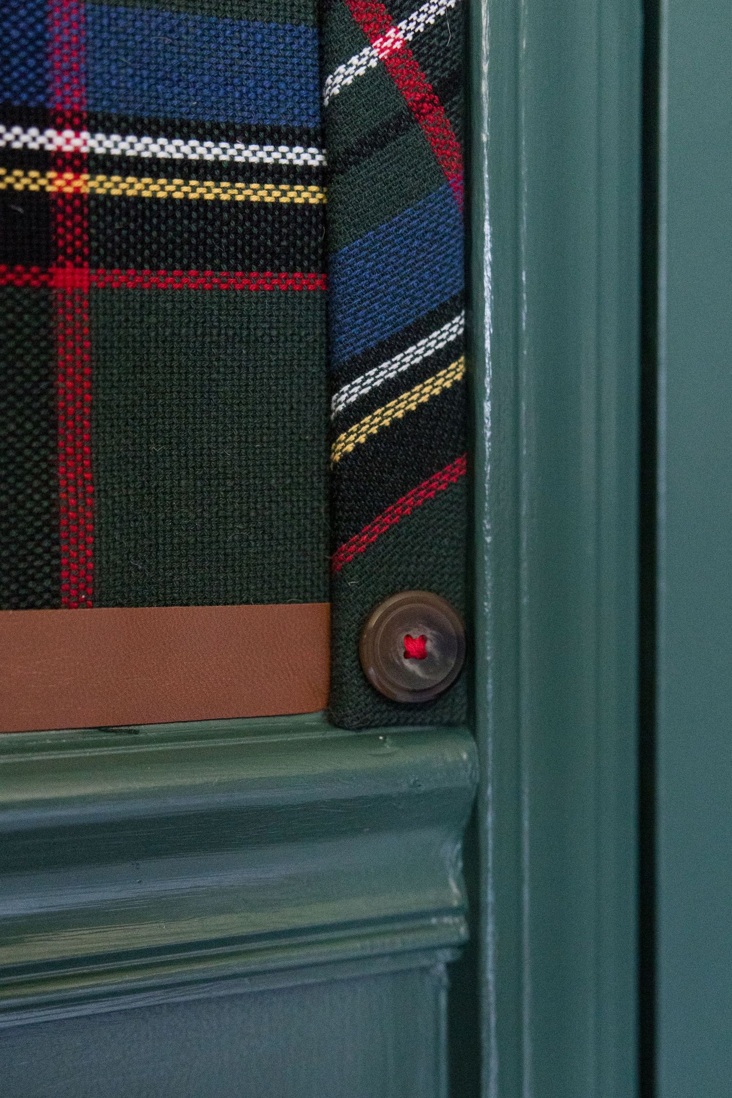 Detail shot of plaid fabric and leather wallet with a dark green door frame.