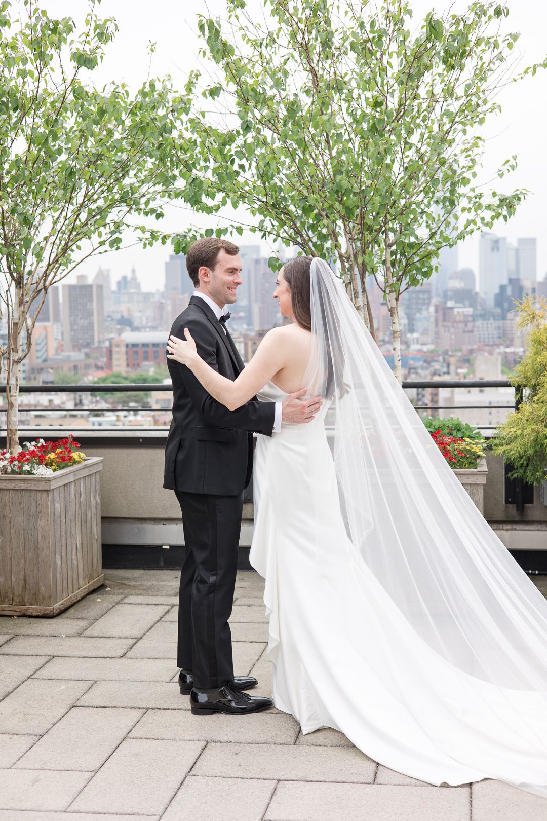 A newlywed couple embraces on an elegant rooftop terrace with Manhattan skyscrapers in the background.