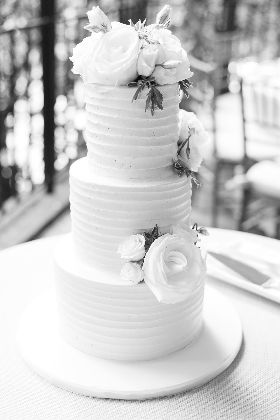 Three-tiered white wedding cake decorated with fresh roses and textured horizontal lines.