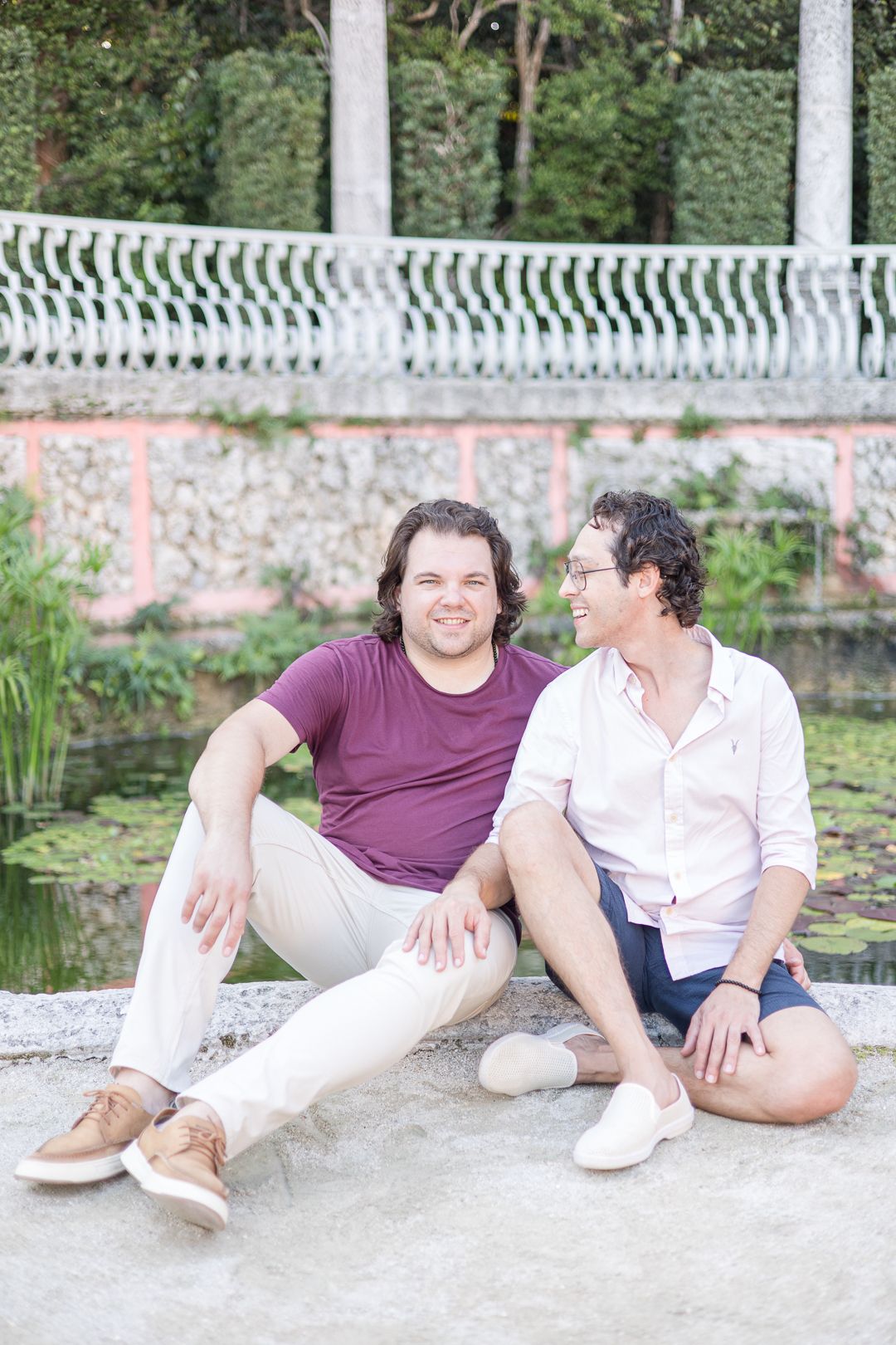 A couple sits together on a stone ledge by a pond at a historic estate.