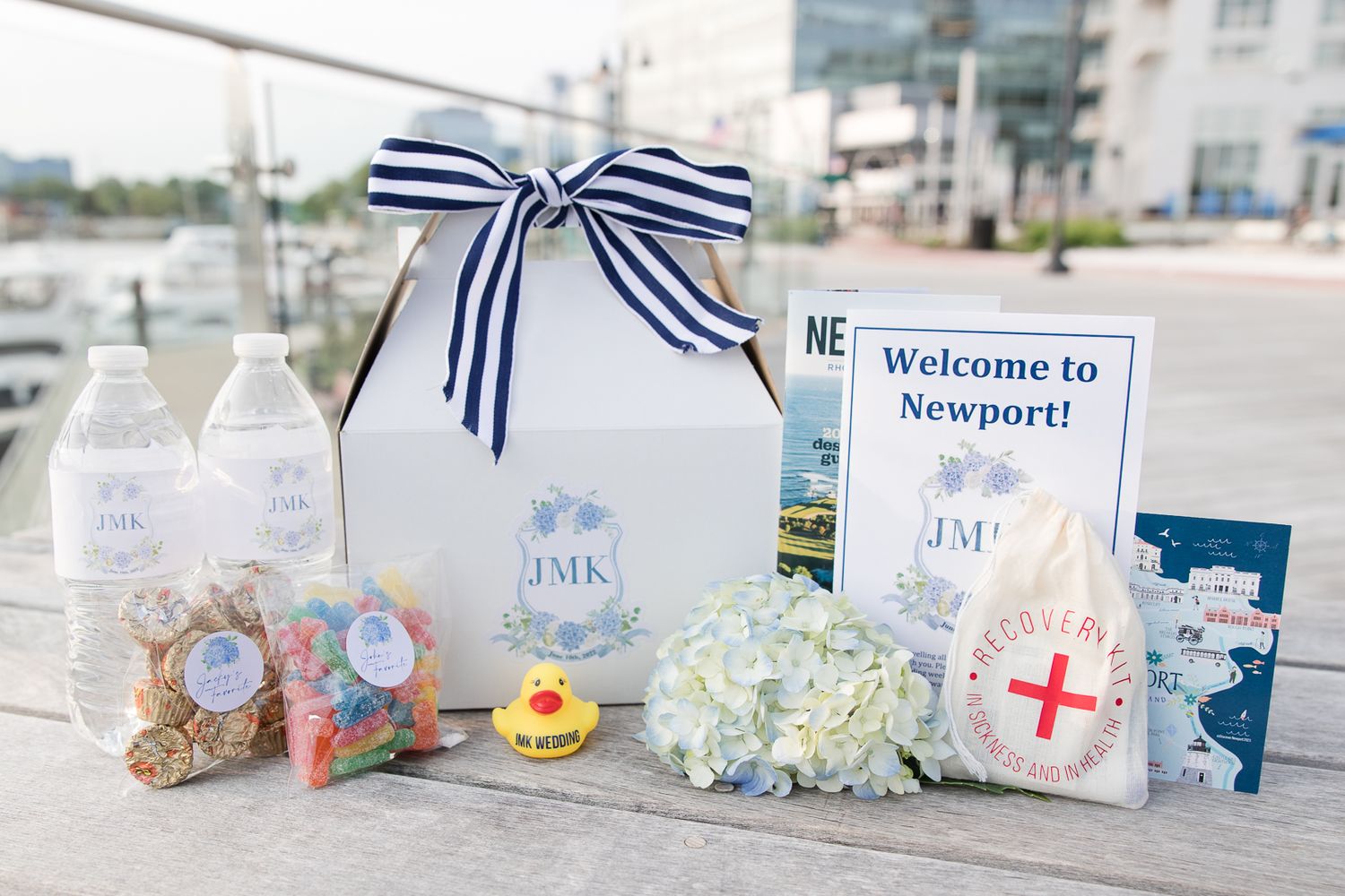Newport welcome gift box with striped bow, water bottles, and hydrangeas on wooden deck.
