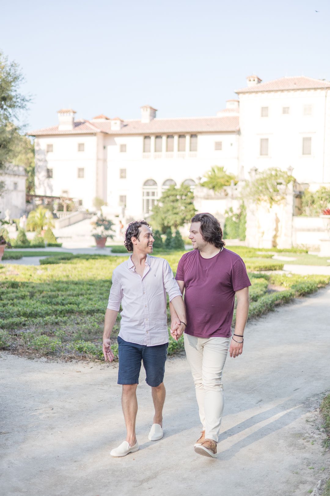 Two people walking hand in hand on a path near an elegant Mediterranean villa.