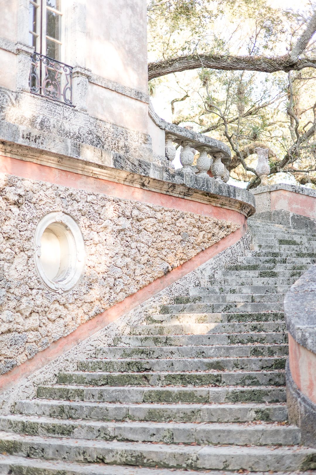 Stone staircase with weathered pink walls and decorative balustrades winds up through a garden setting.