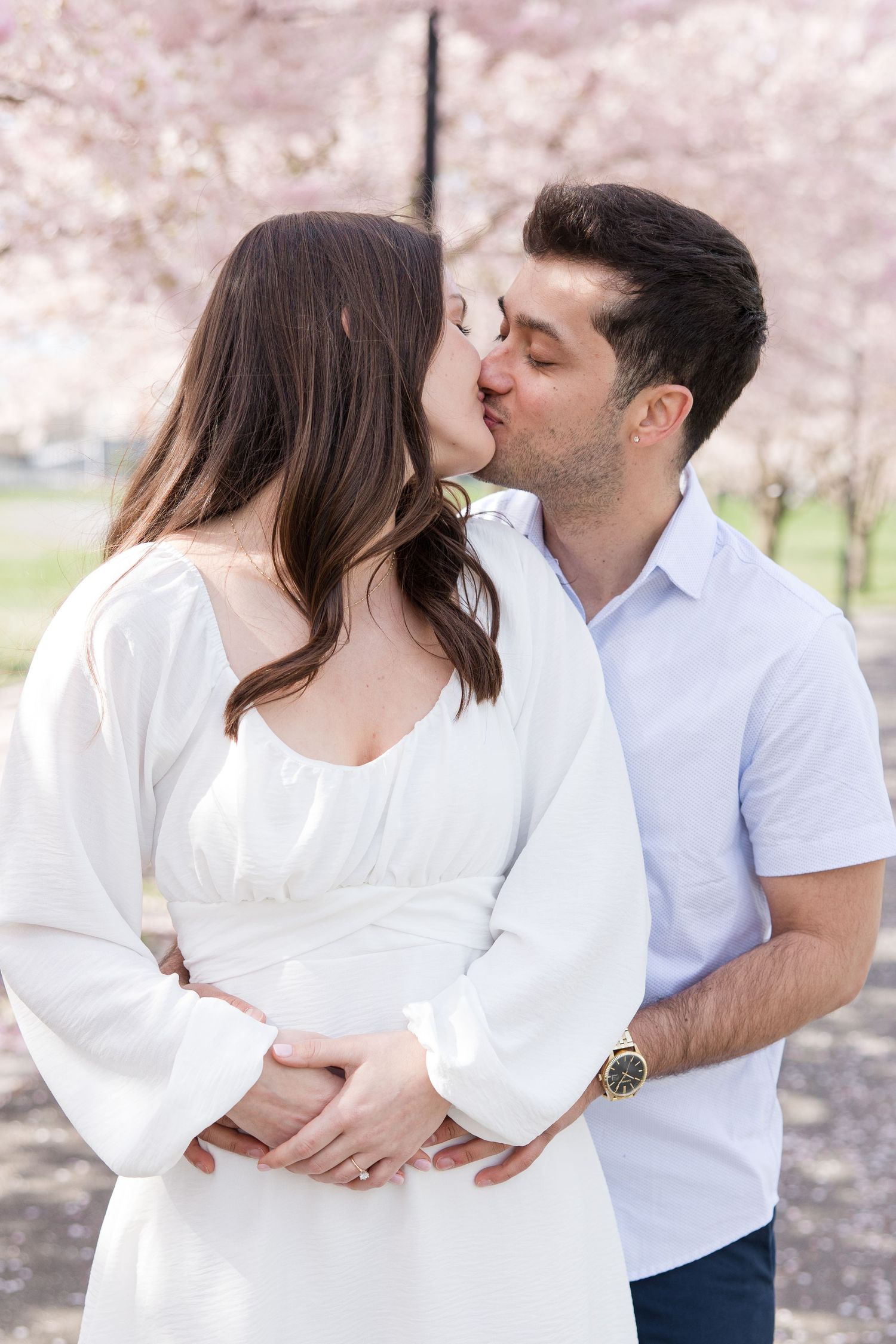 Romantic couple kissing under blooming cherry blossom trees in springtime.