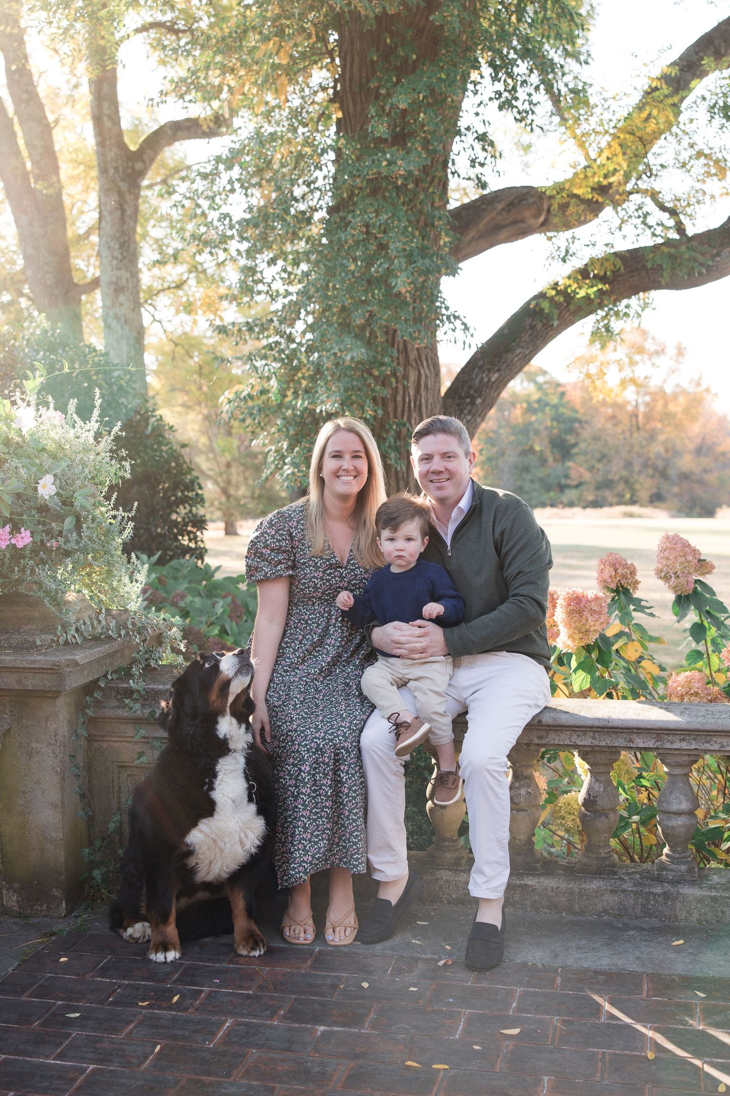 A family sitting together on brick steps with autumn trees in the background and warm sunlight filtering through.