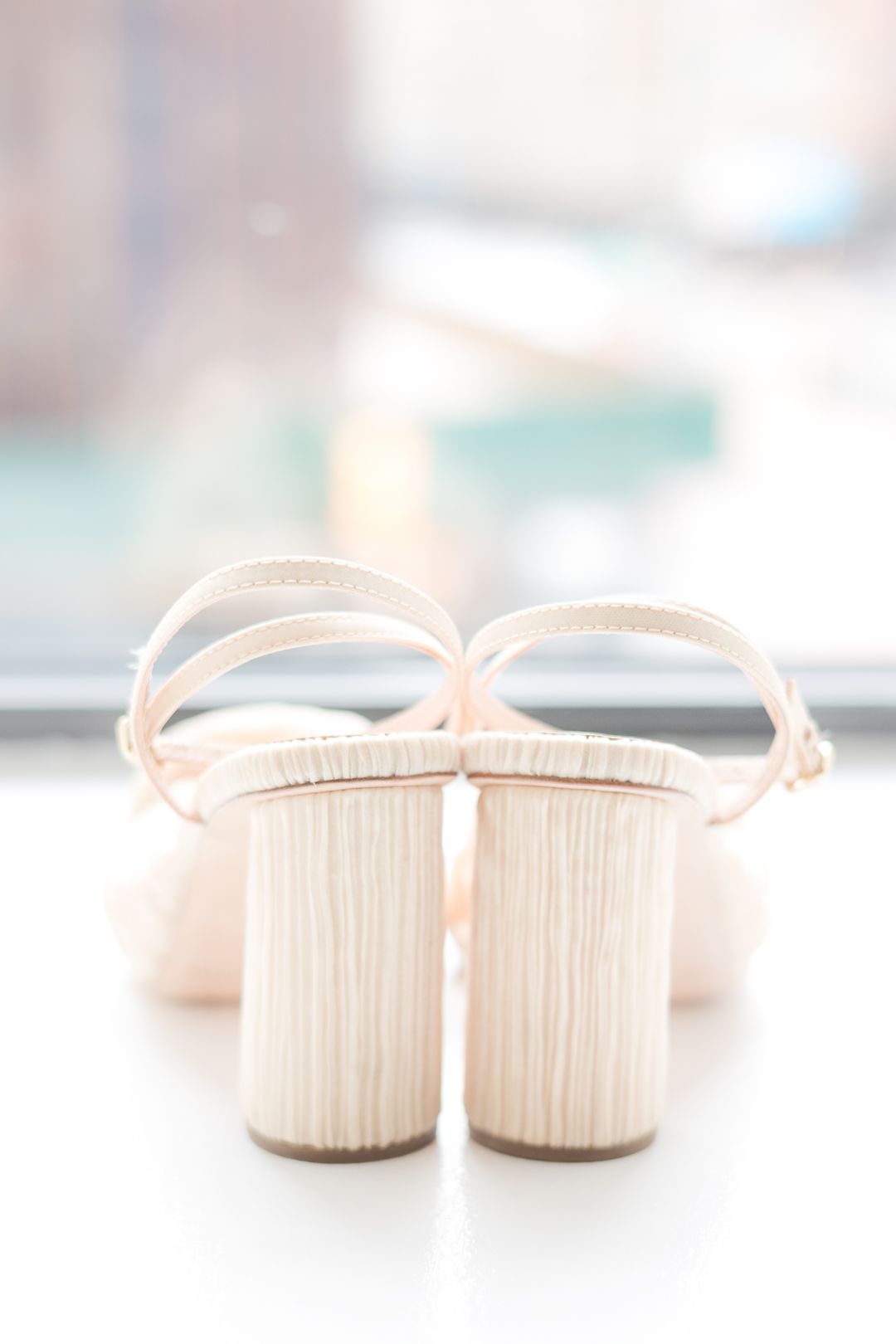 Cream colored bridal shoes with block heels photographed from behind.
