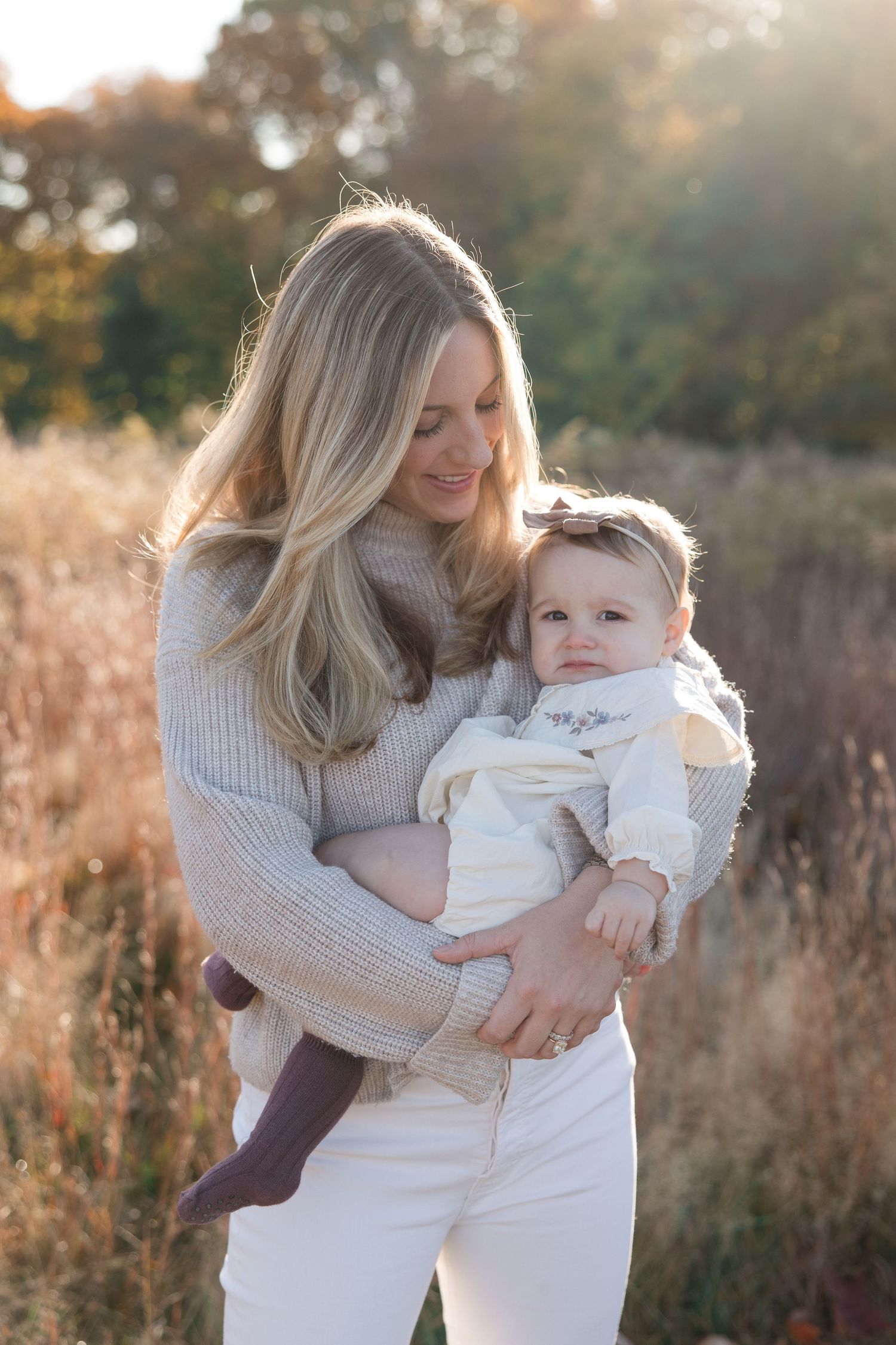 Sweet outdoor portrait of caregiver holding baby in knit sweater against autumn field.