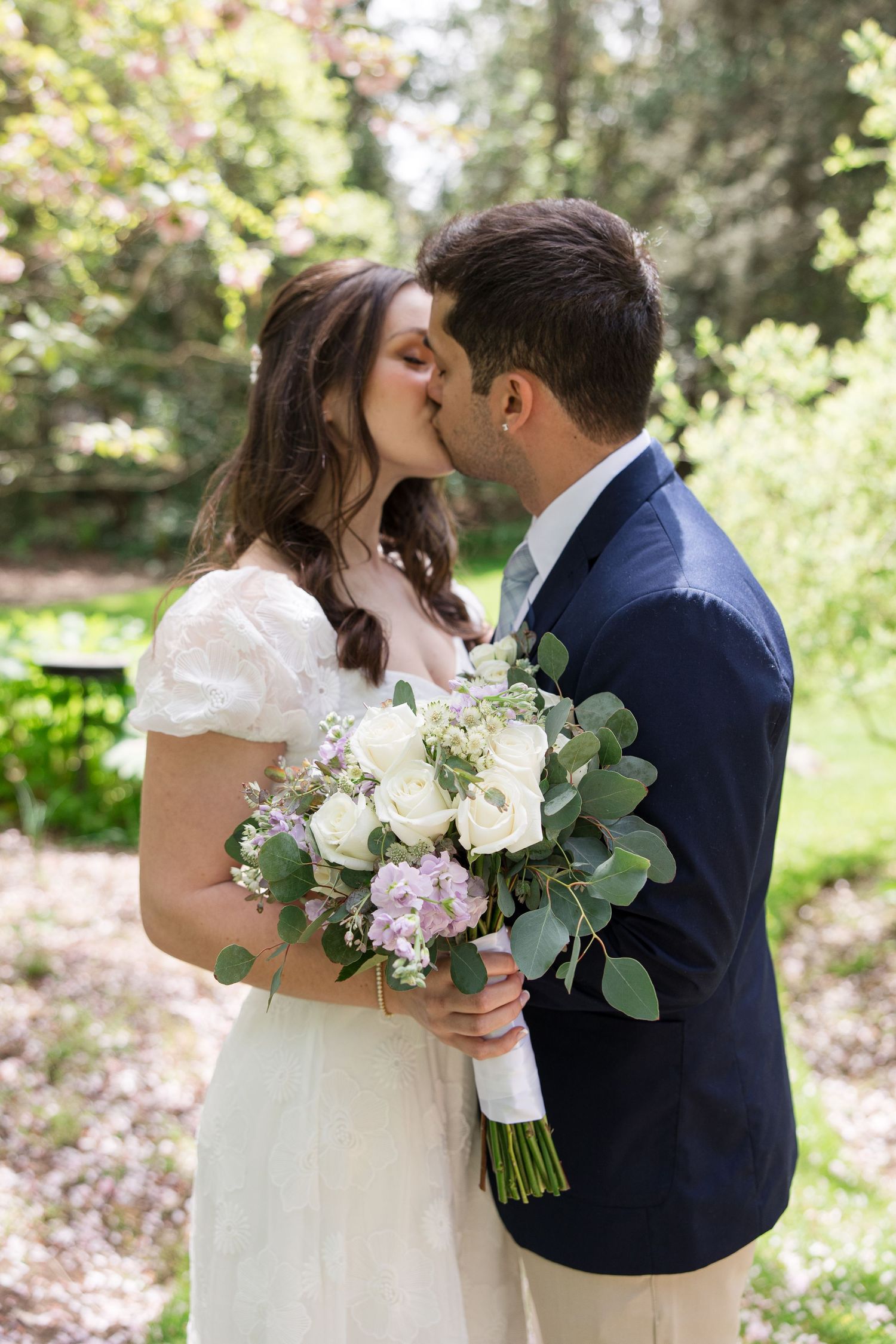 A romantic wedding photo showing a couple kissing in a garden setting with a floral bouquet.