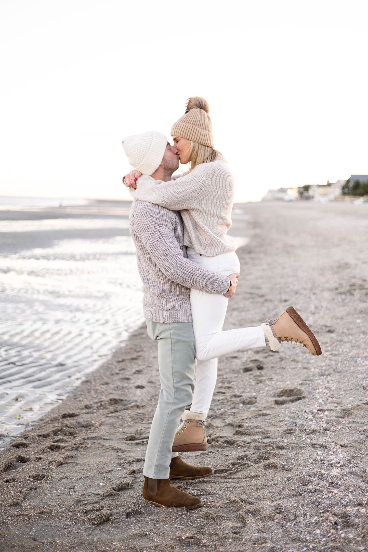 Couple in cozy sweaters embracing on winter beach.