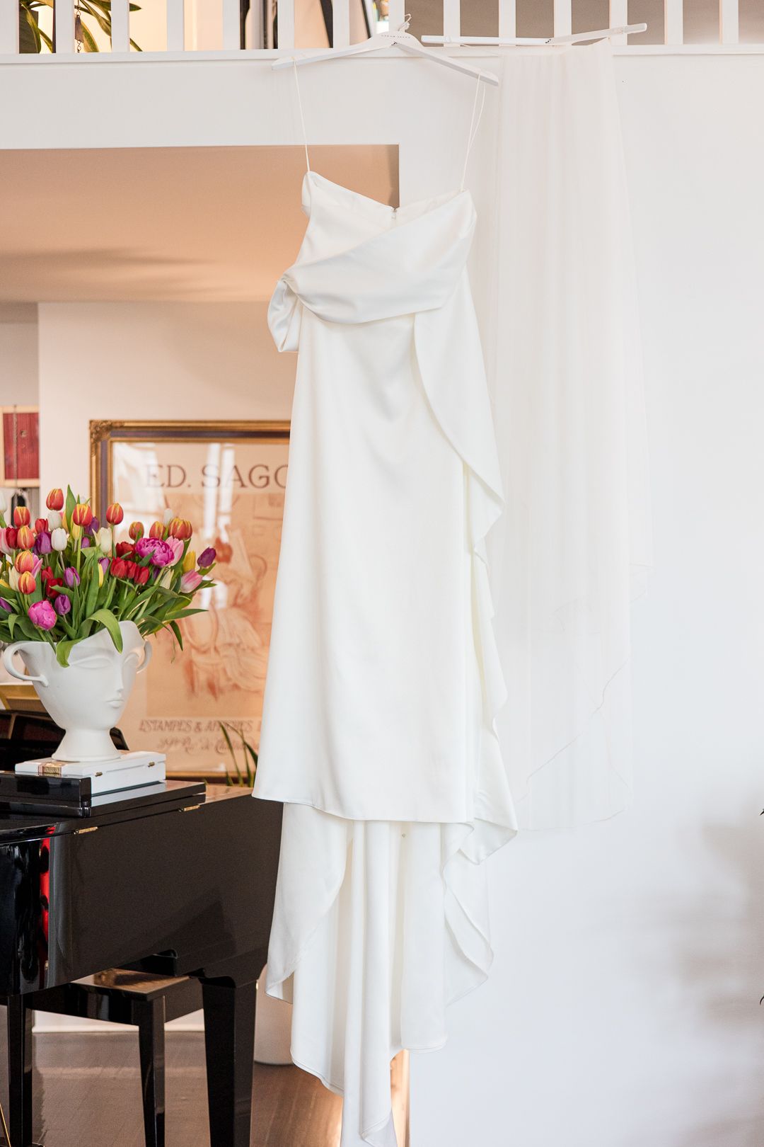White wedding gown displayed against peach wall with tulips and piano decor.