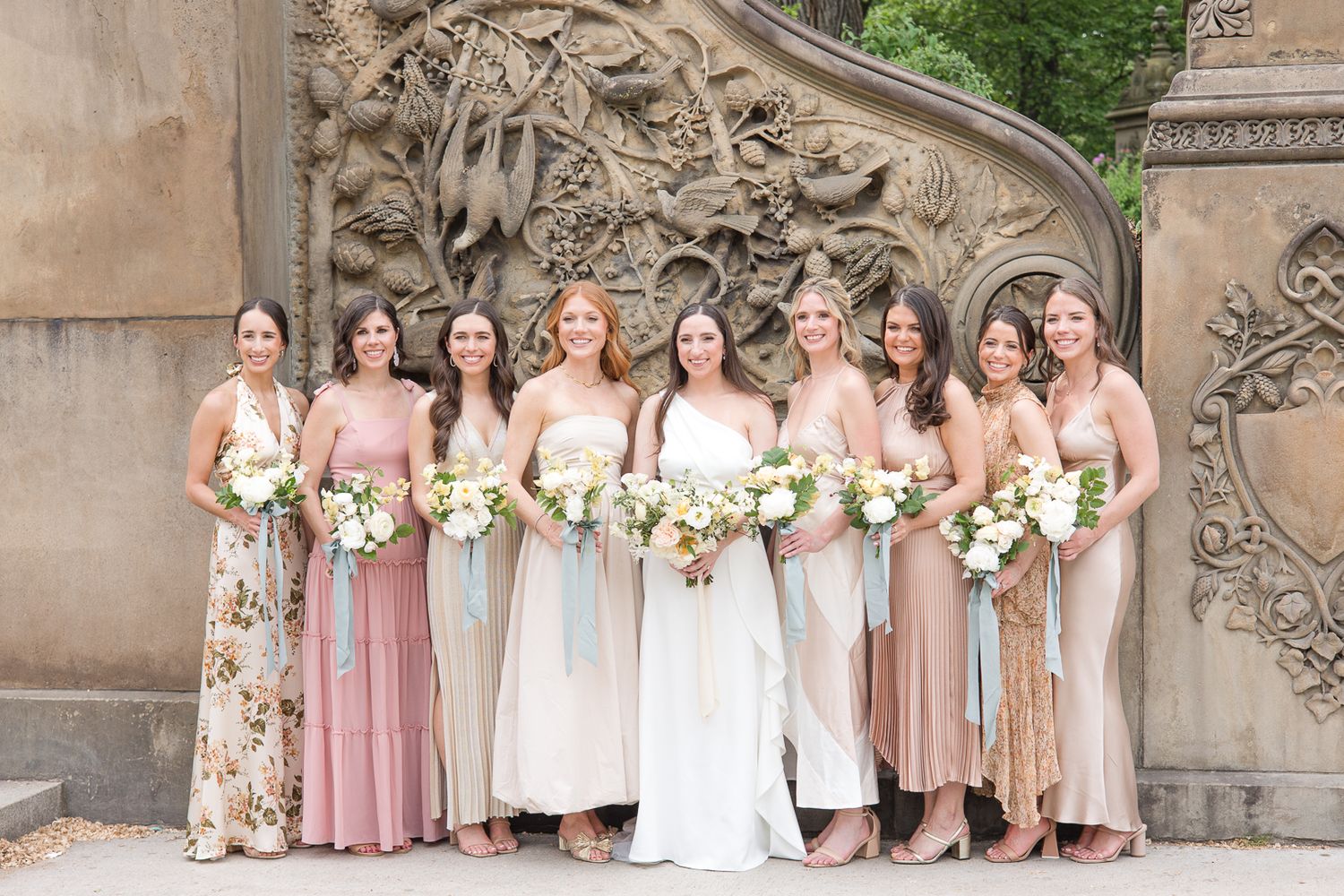 Bridesmaids in pink and floral dresses posed against ornate stone architectural backdrop.