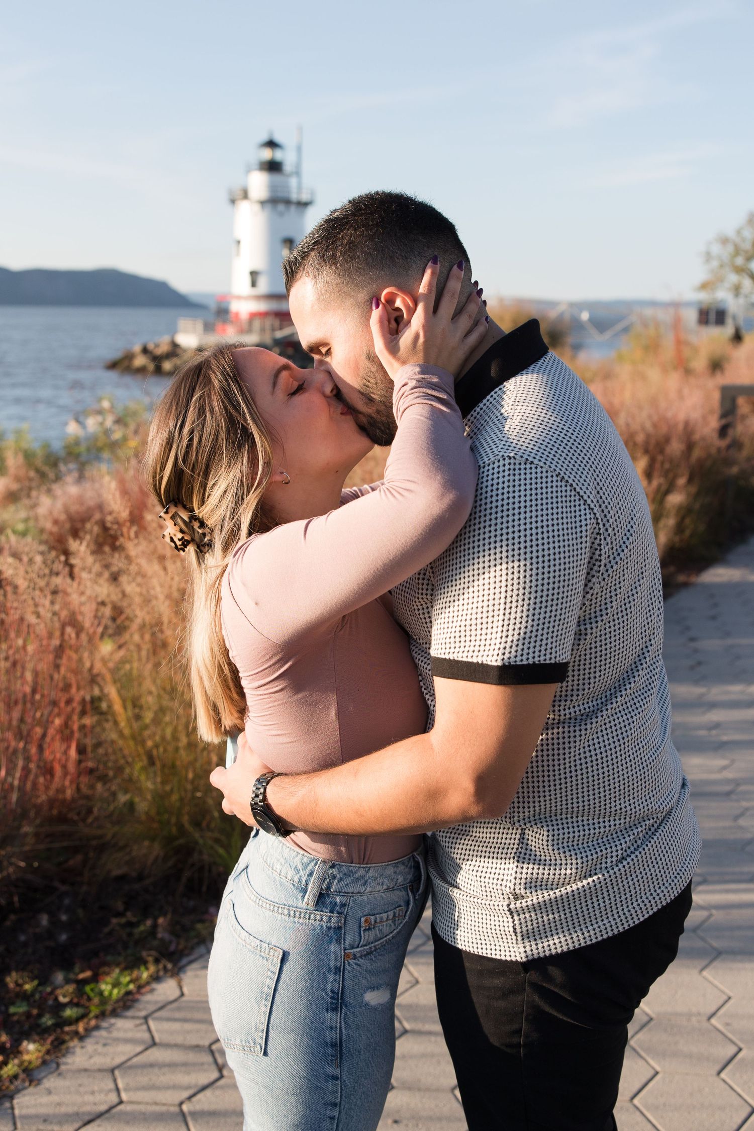 Intimate moment between a couple embracing near a lighthouse with water views.