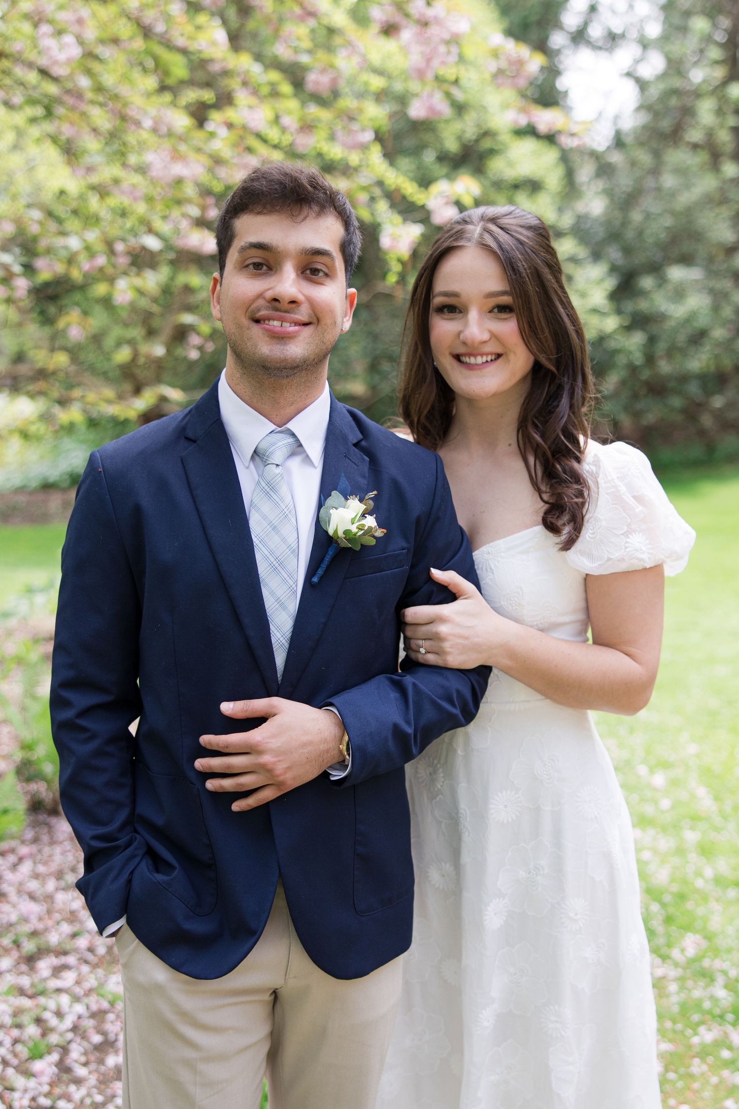 Happy newlyweds pose together in spring garden with blooming trees.