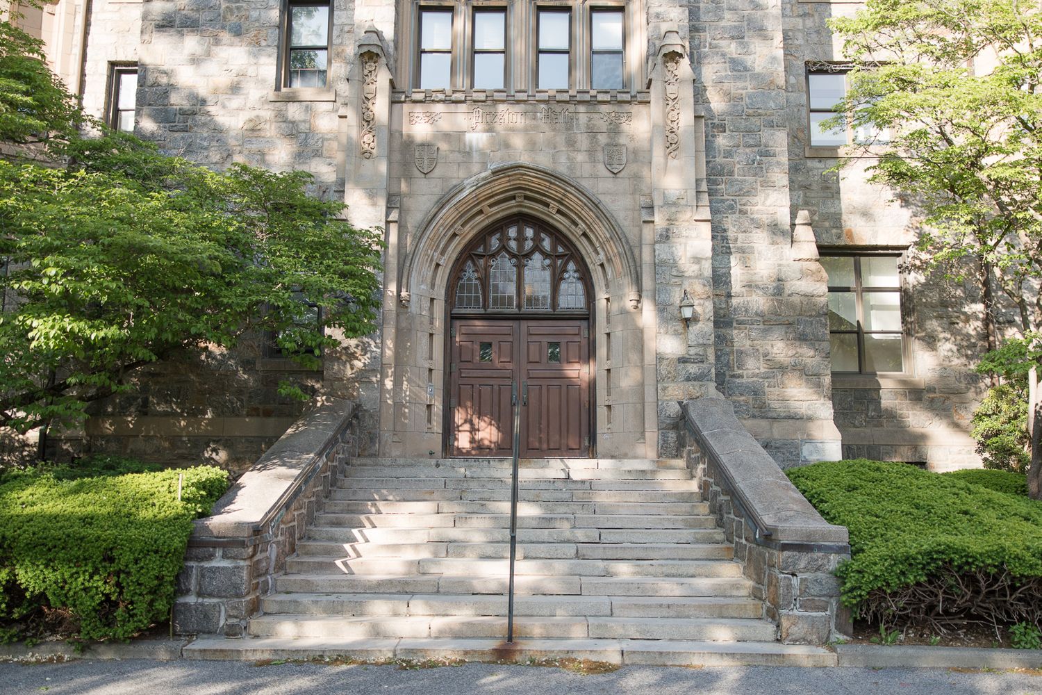 Gothic stone archway entrance with steps leading to wooden doors surrounded by greenery.