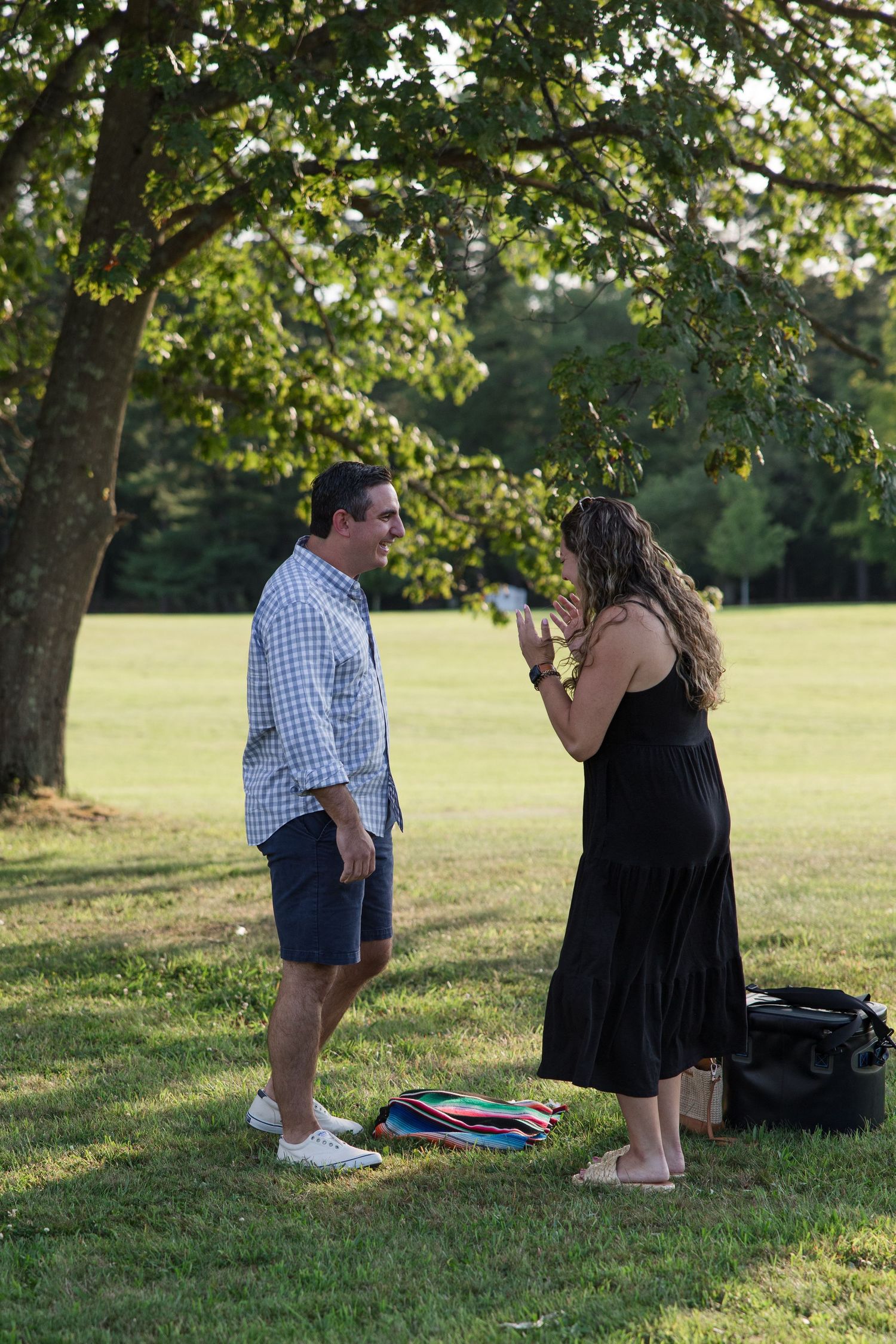 A couple in casual summer attire having a conversation in a park under tree branches.