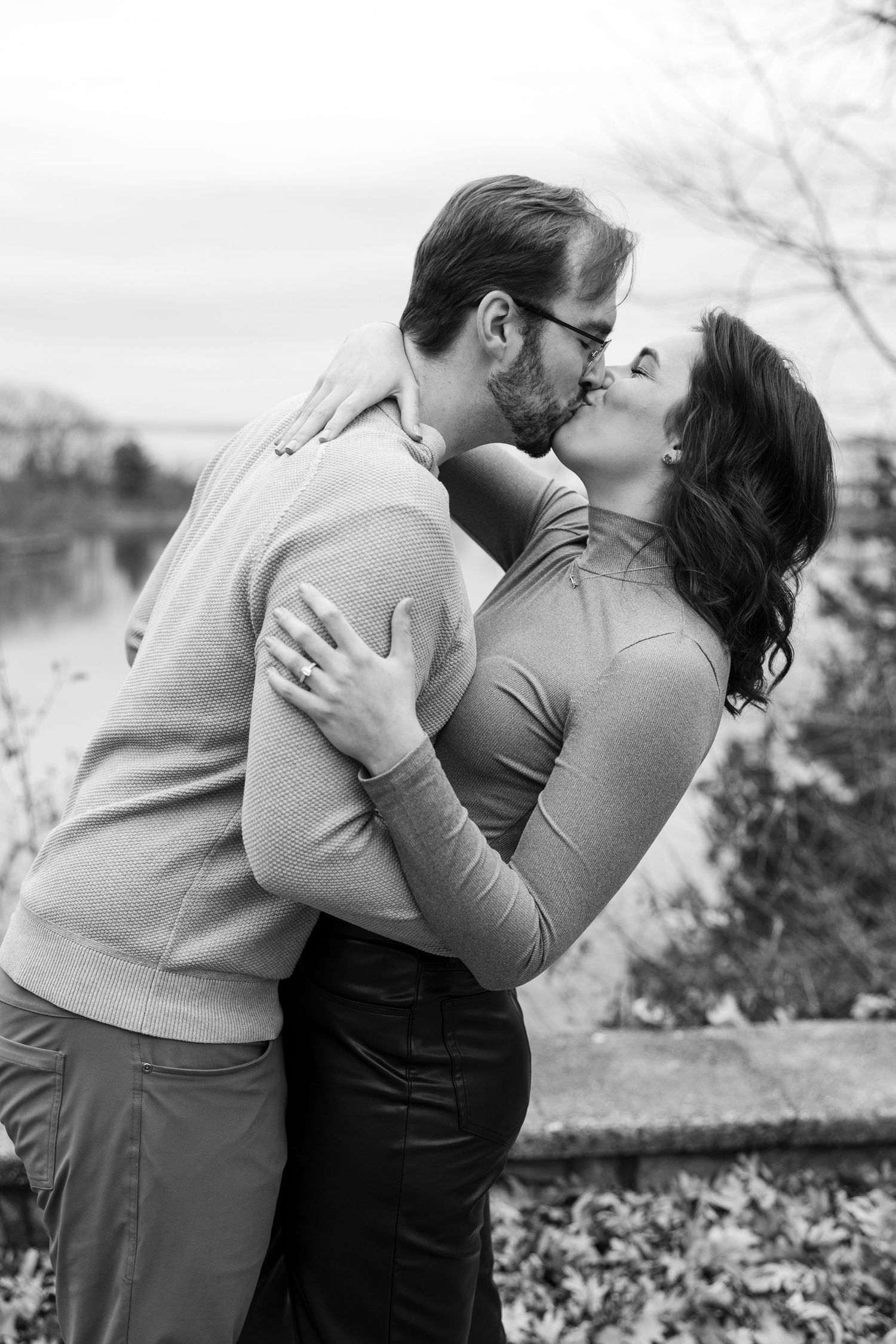 A romantic black and white portrait of a couple sharing a passionate kiss by a lake.