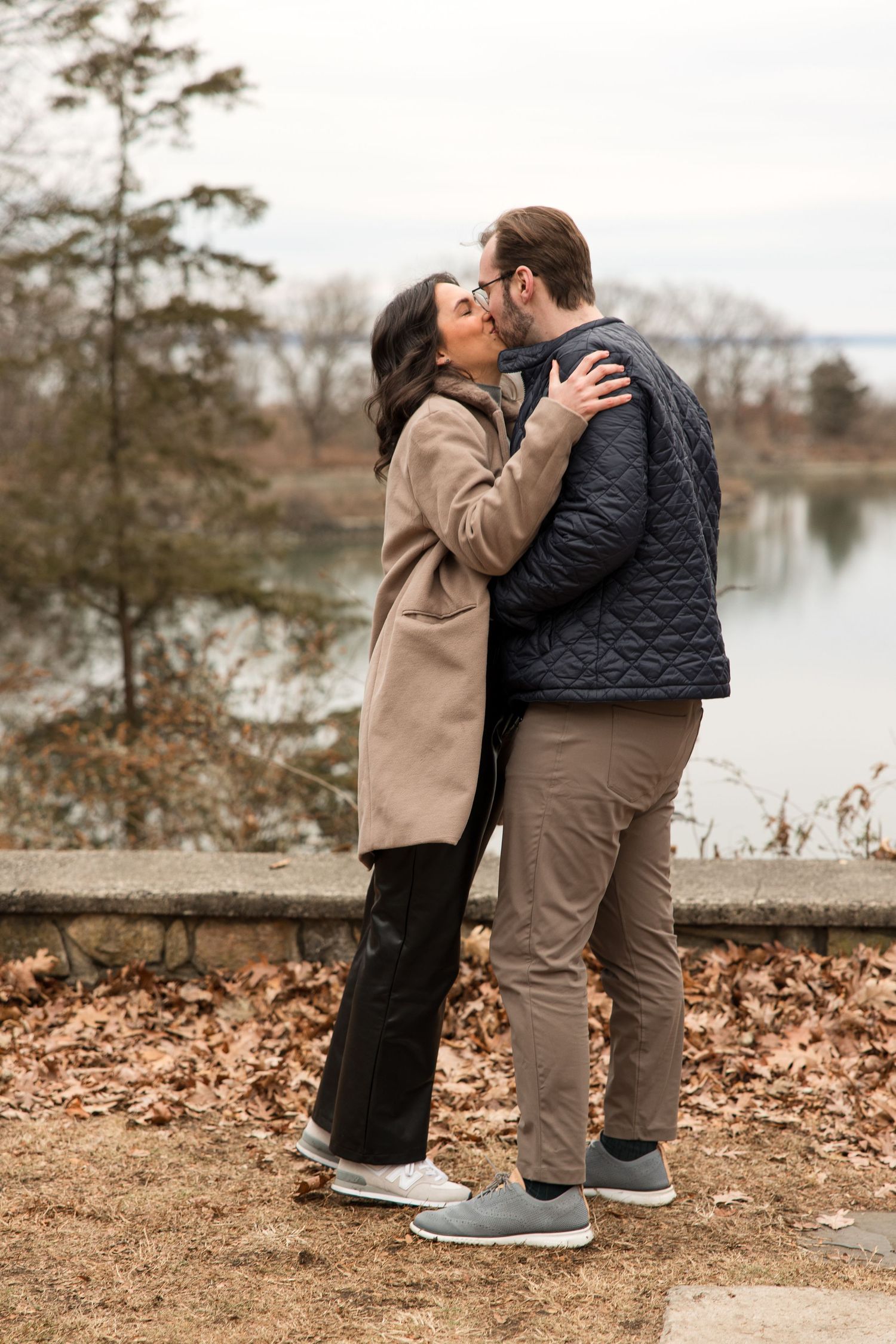 A romantic embrace between a couple wearing coordinating coats by a serene lake.
