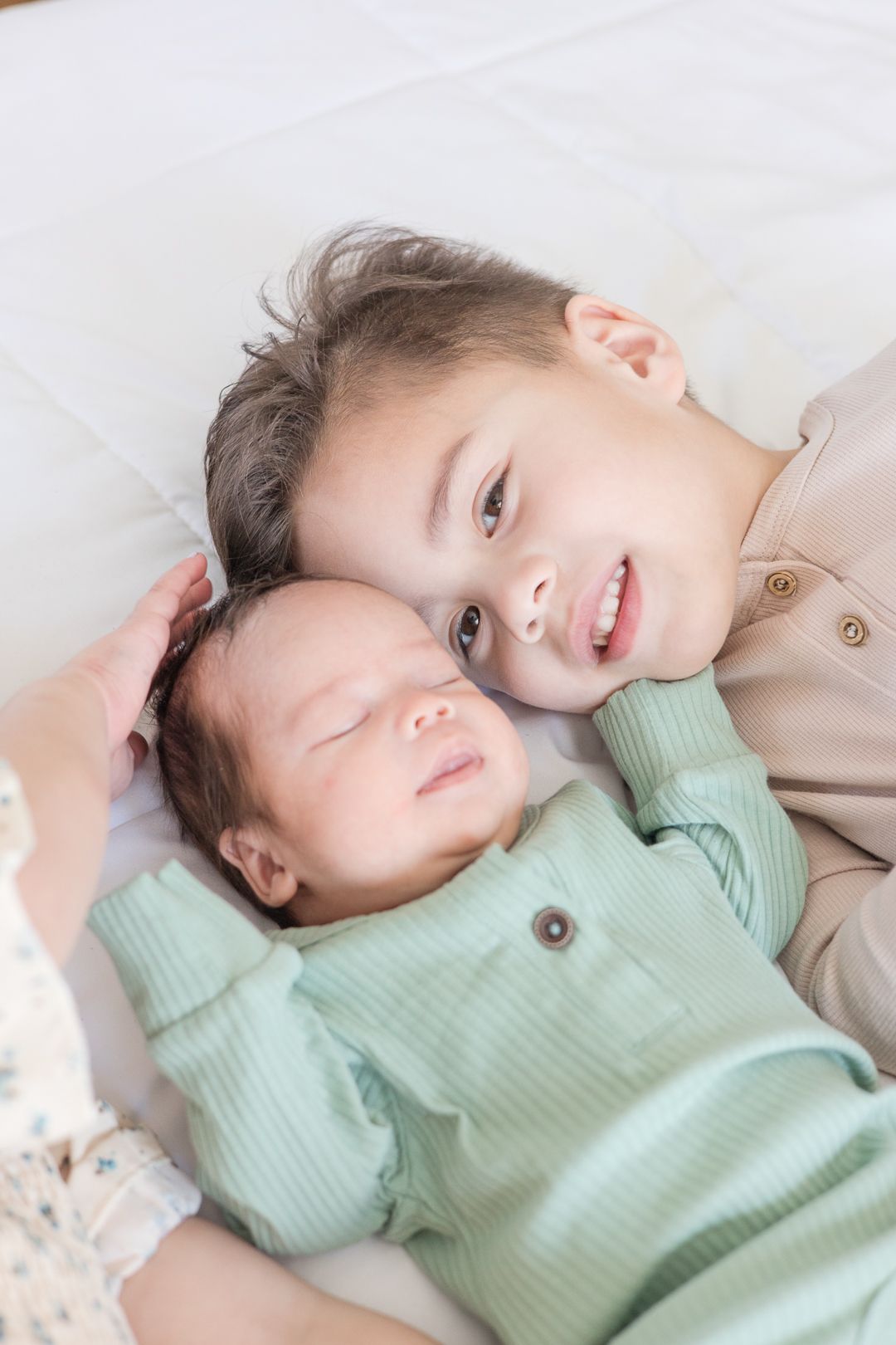 Two siblings in matching button-up outfits share a tender moment on white bedding.
