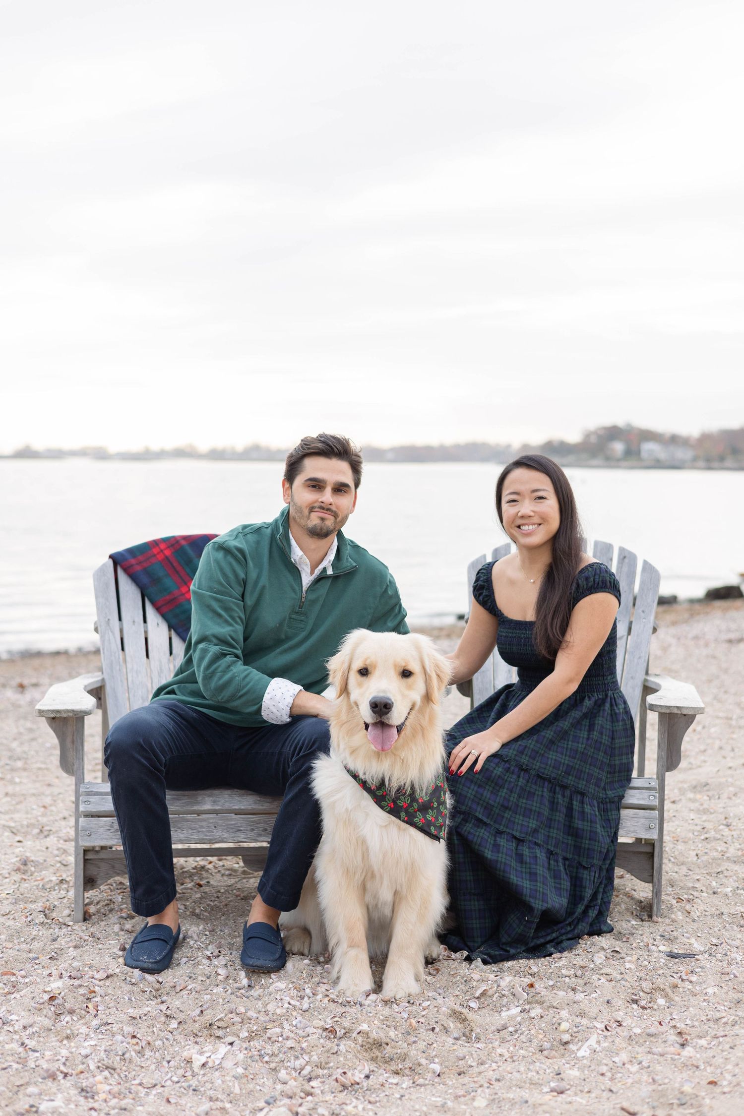 A couple sits in an Adirondack chair with their golden retriever by the waterfront.