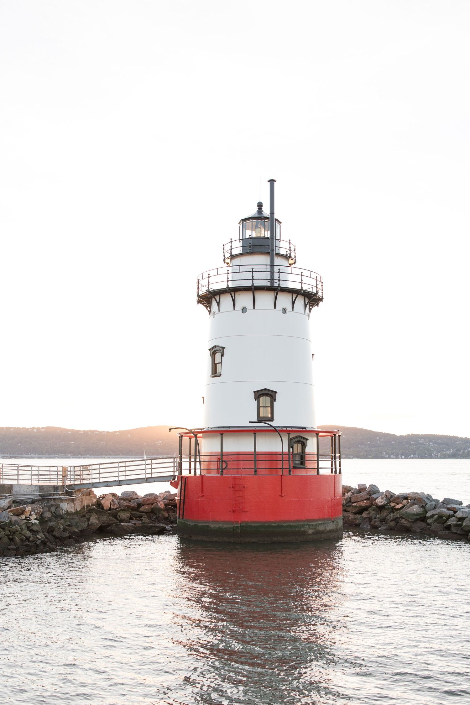Red and white lighthouse standing on rocky breakwater during sunset.