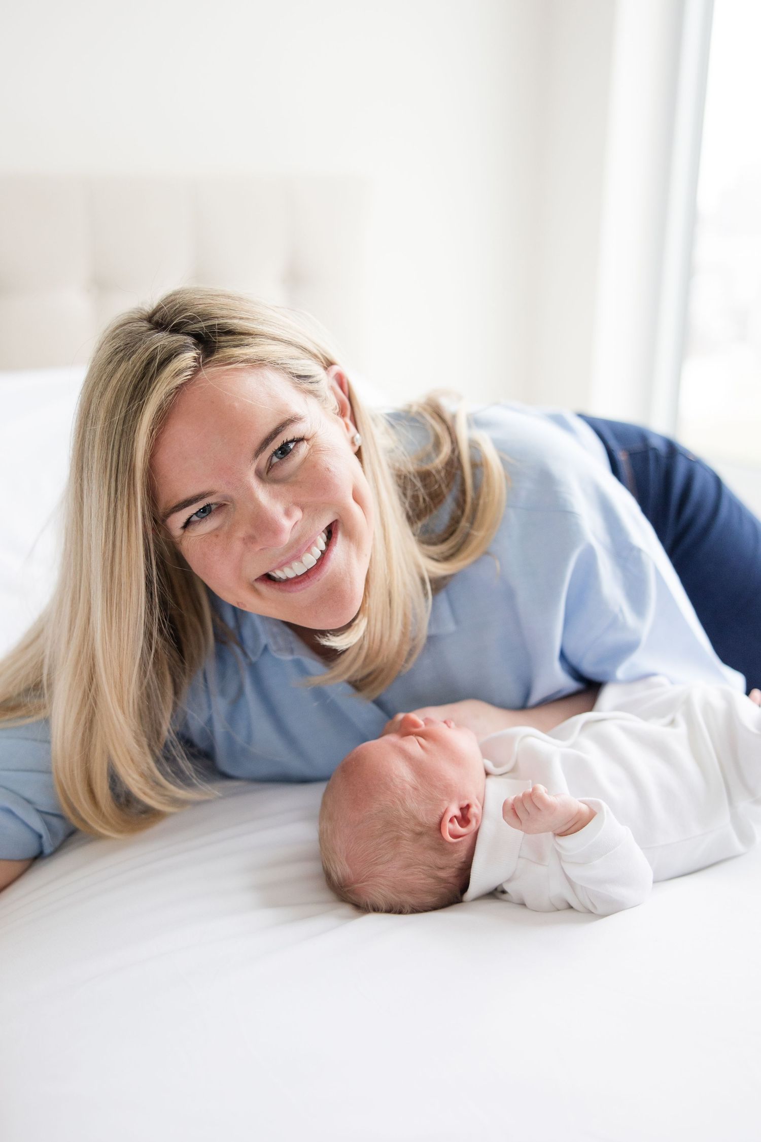 Parent and newborn baby laying together on white bedding while sharing a tender moment.