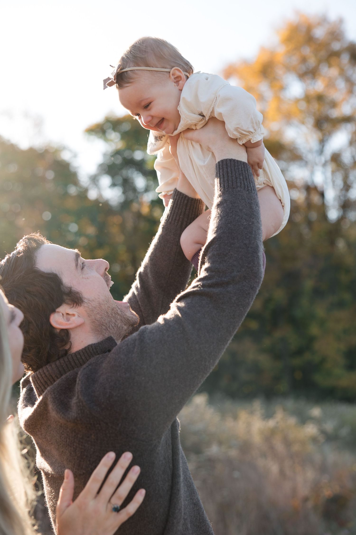 Joyful moment of parent lifting baby in air during sunset outdoors.