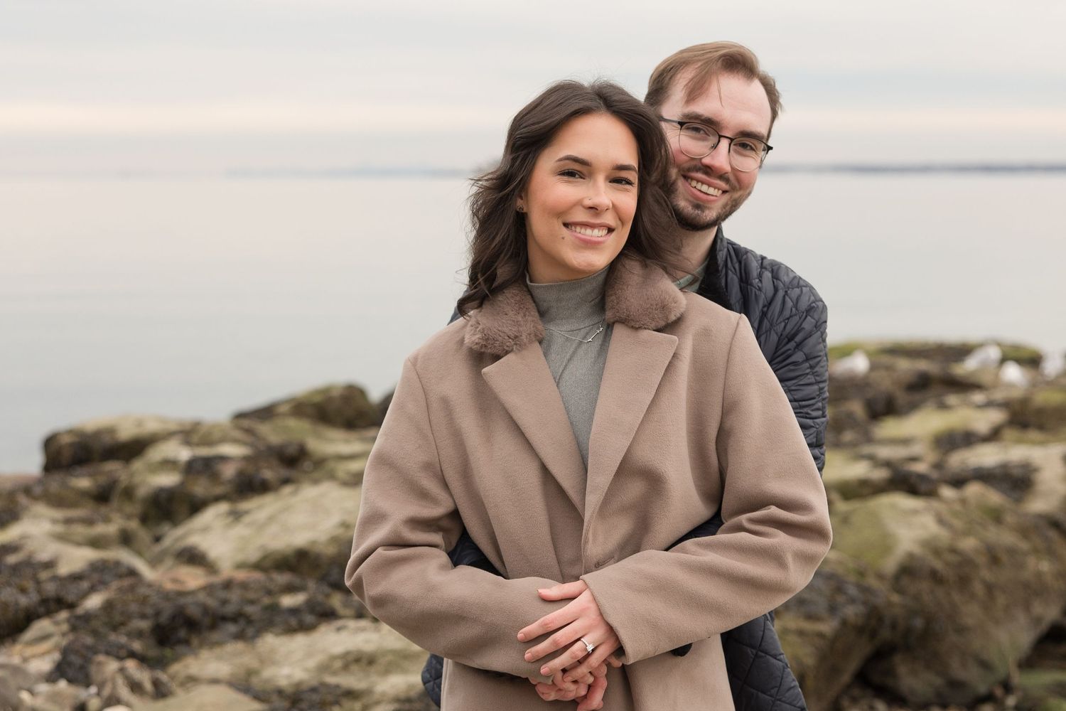 A couple embracing on a rocky coastline during sunset.