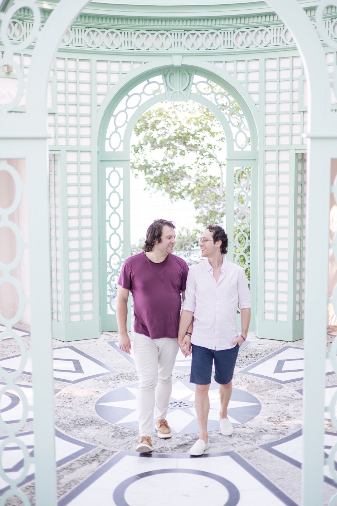 Two people walking under ornate mint green gazebo with decorative lattice design.