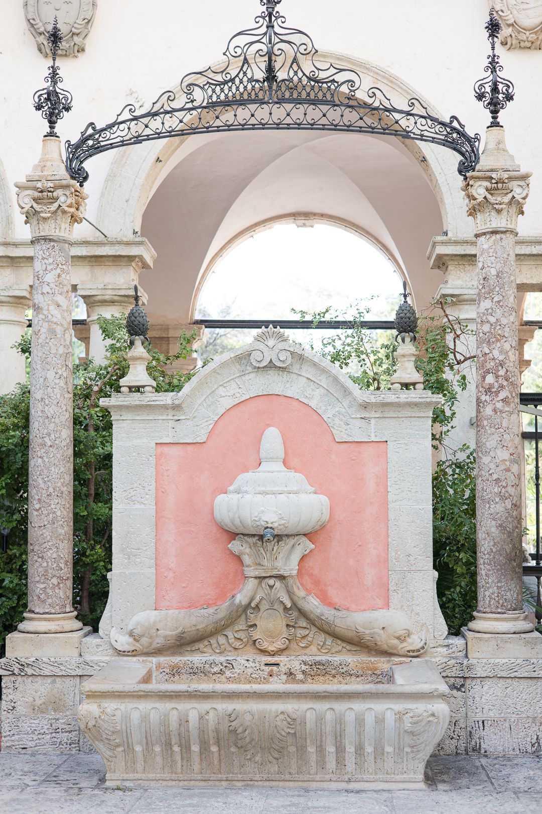 Ornate stone fountain with decorative iron archway and coral pink accent wall.