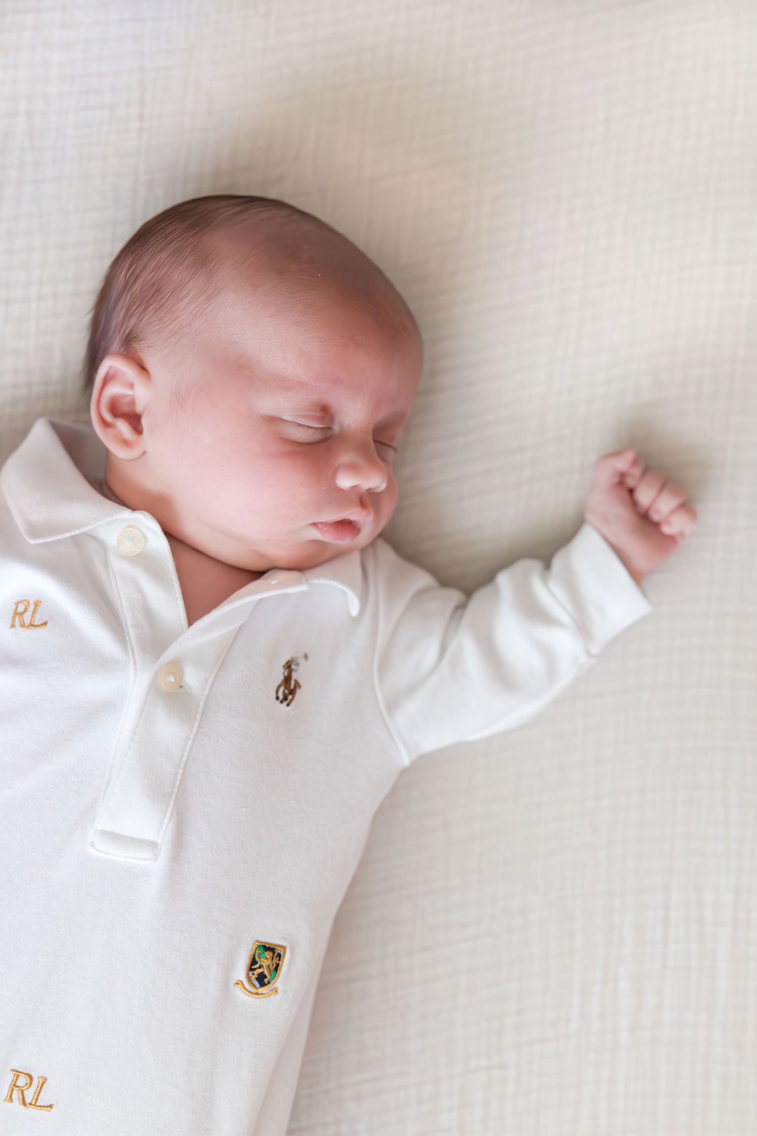 Sleeping baby wearing a white Ralph Lauren polo outfit on white bedding.