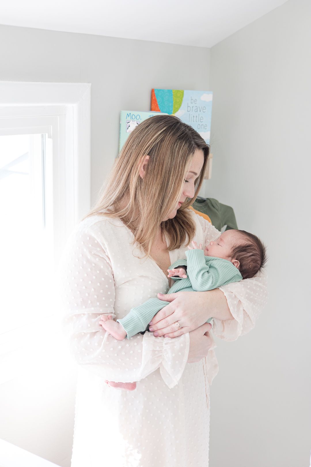 A tender moment with parent and newborn baby in soft natural light wearing pale pink and mint green.