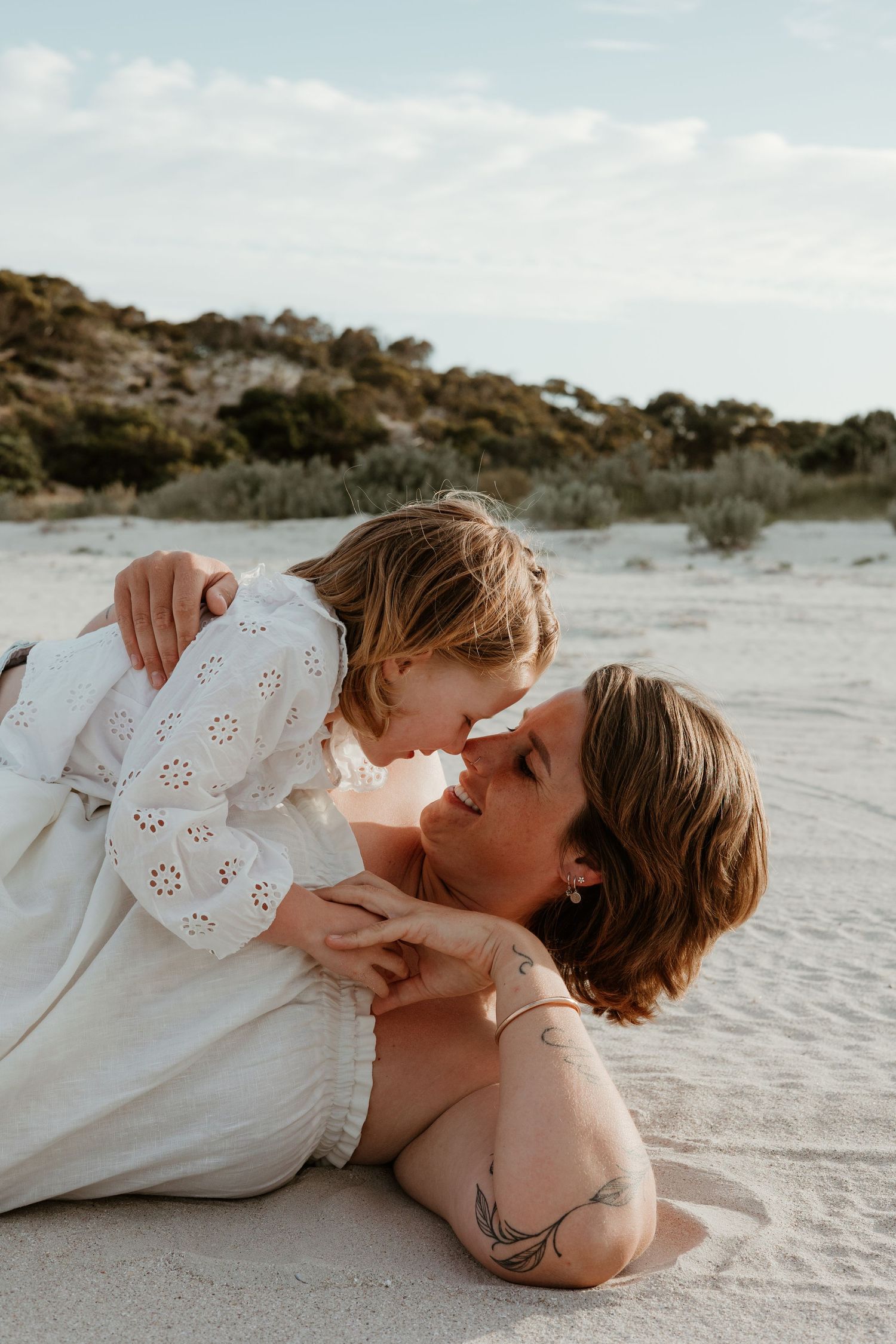 Intimate portrait of a tender moment between two people lying on sandy beach at sunset.