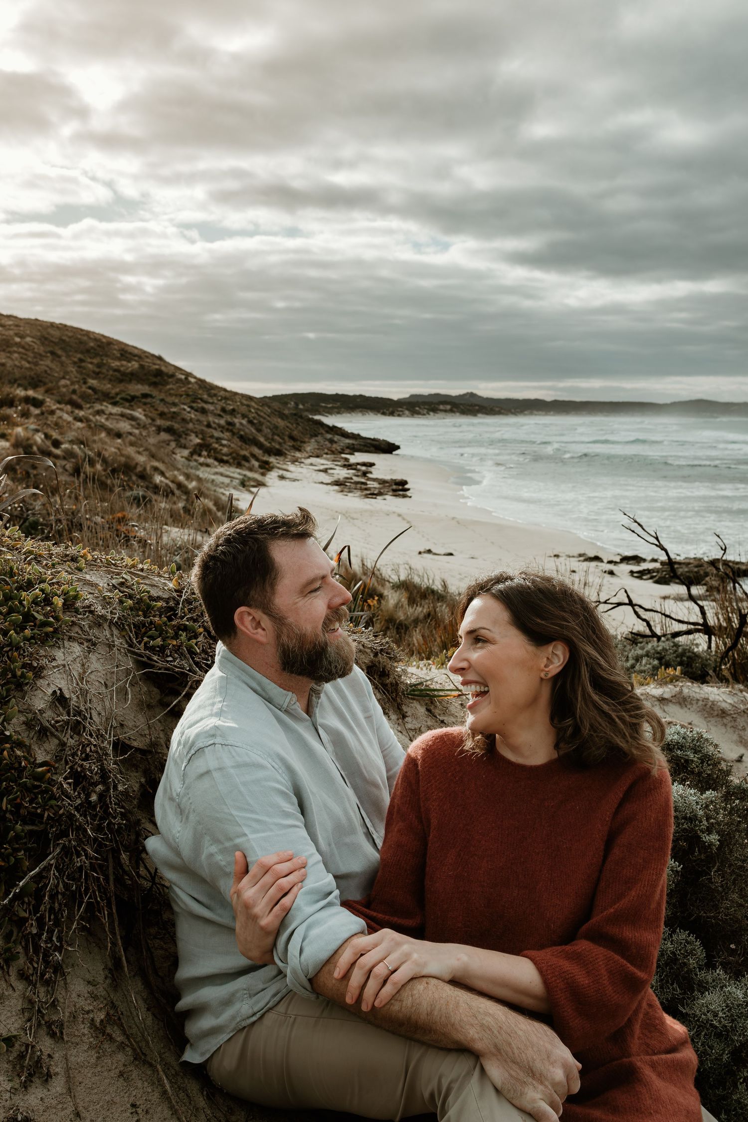 Couple sharing intimate moment on coastal cliff overlooking stormy ocean.
