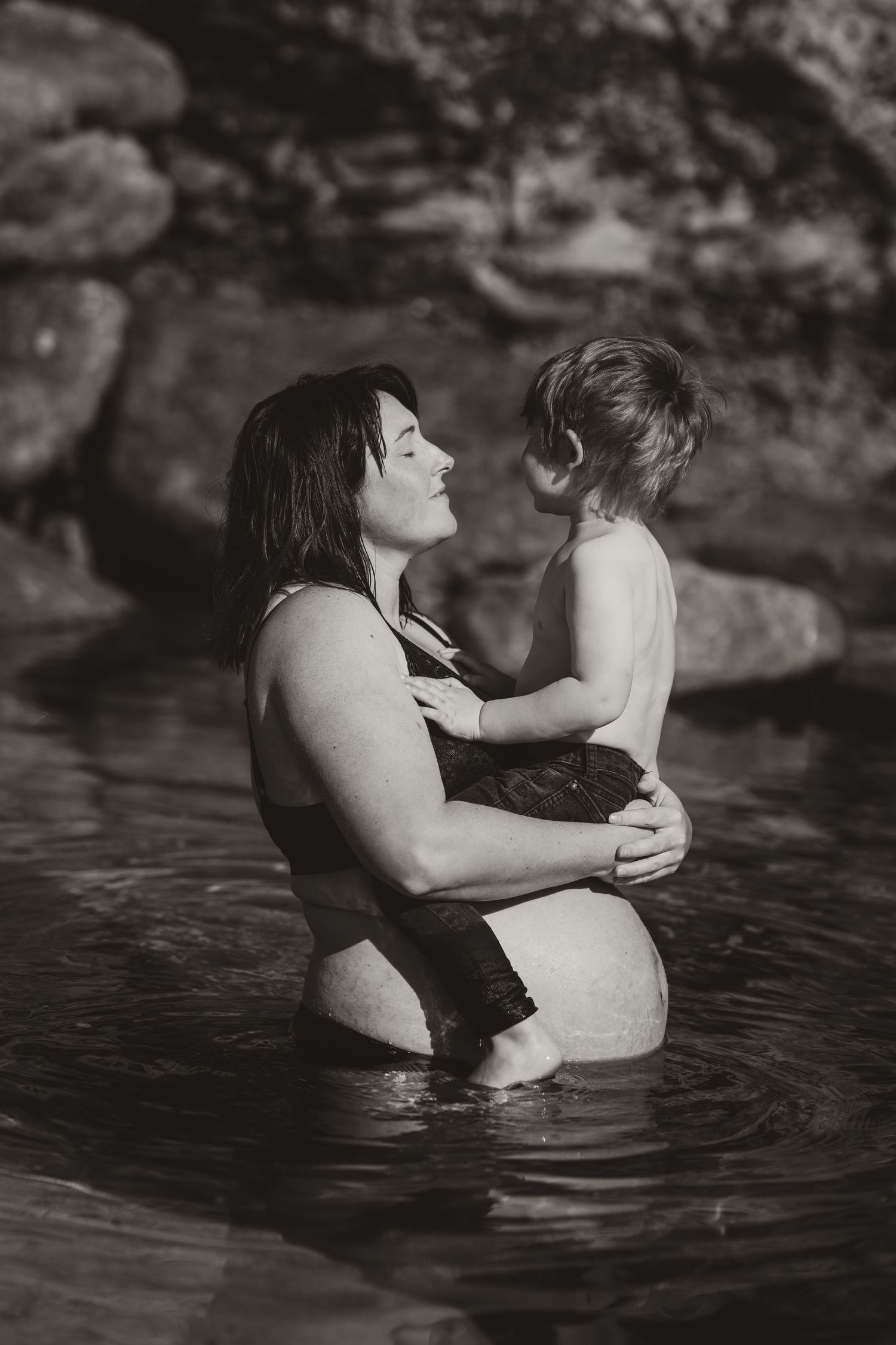 Black and white photo of parent and child sharing a tender moment together in a lake.