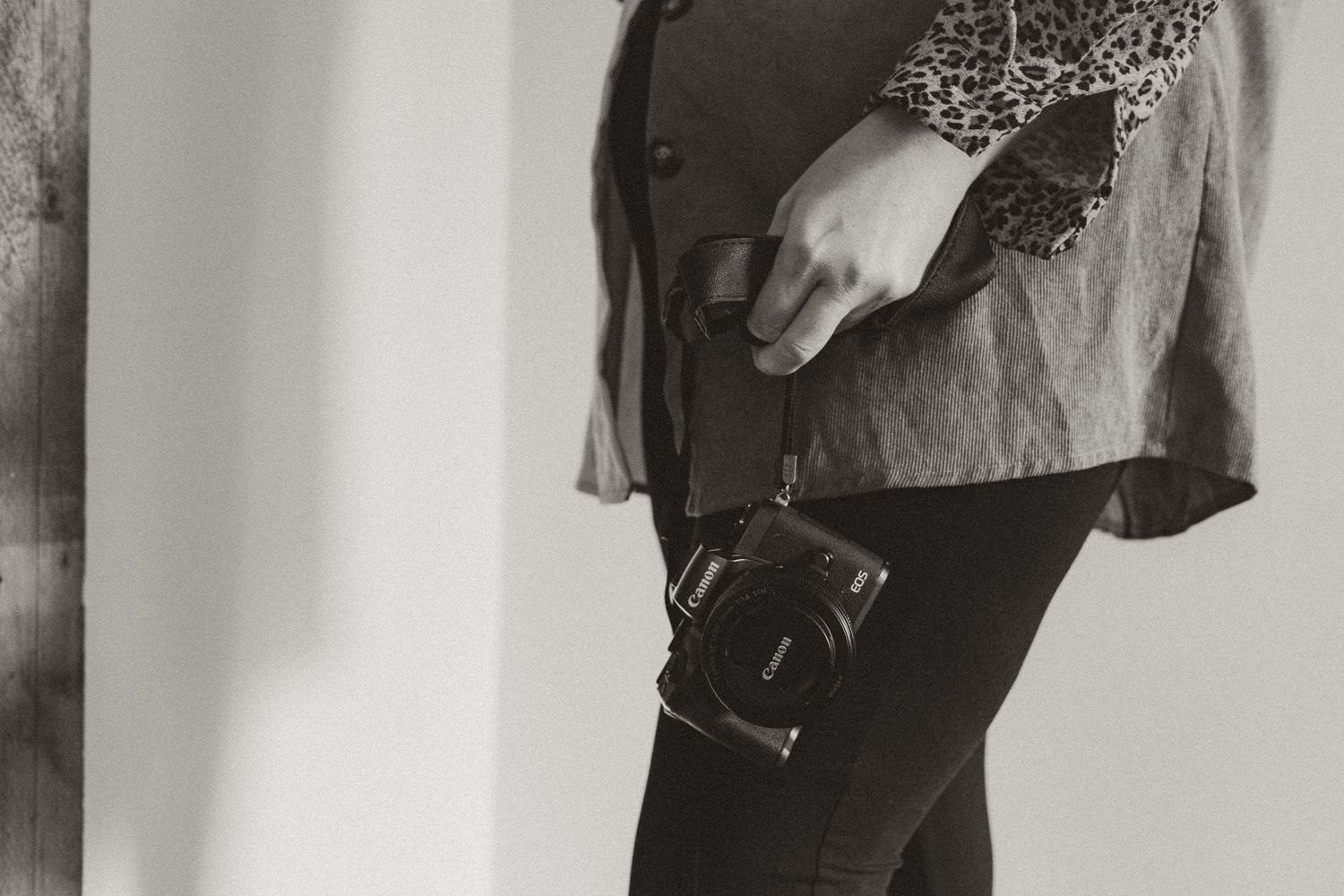 A black and white photo of someone holding a vintage camera against a light colored wall.