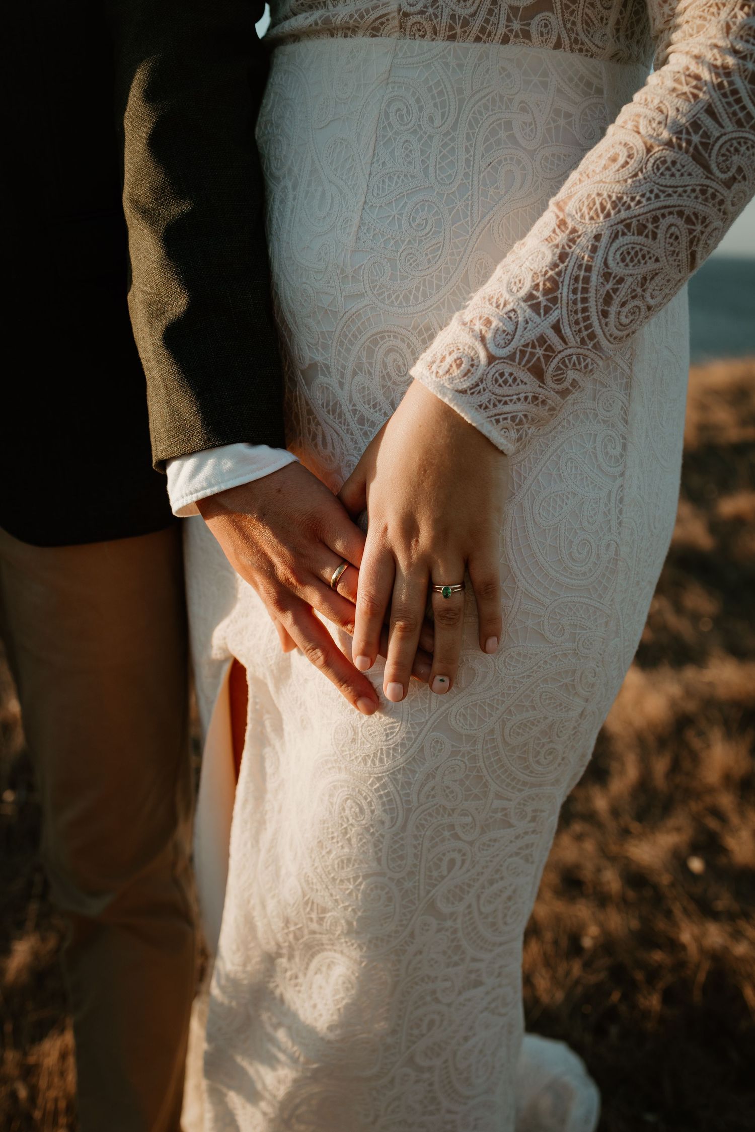 Close-up of couple's hands showing engagement ring against detailed lace wedding dress.