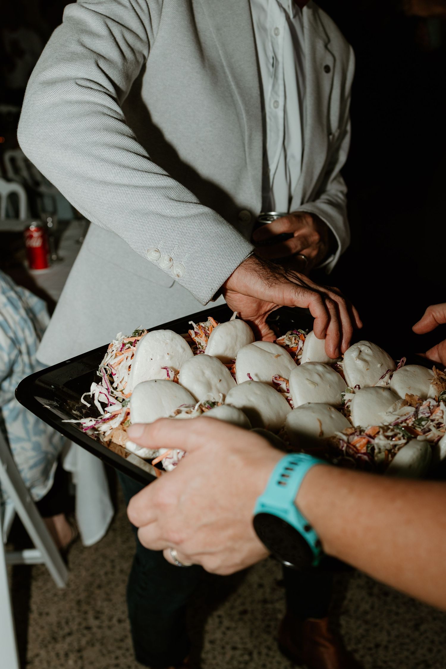 Catered wedding reception food tray filled with sliders being served by staff in a white jacket.