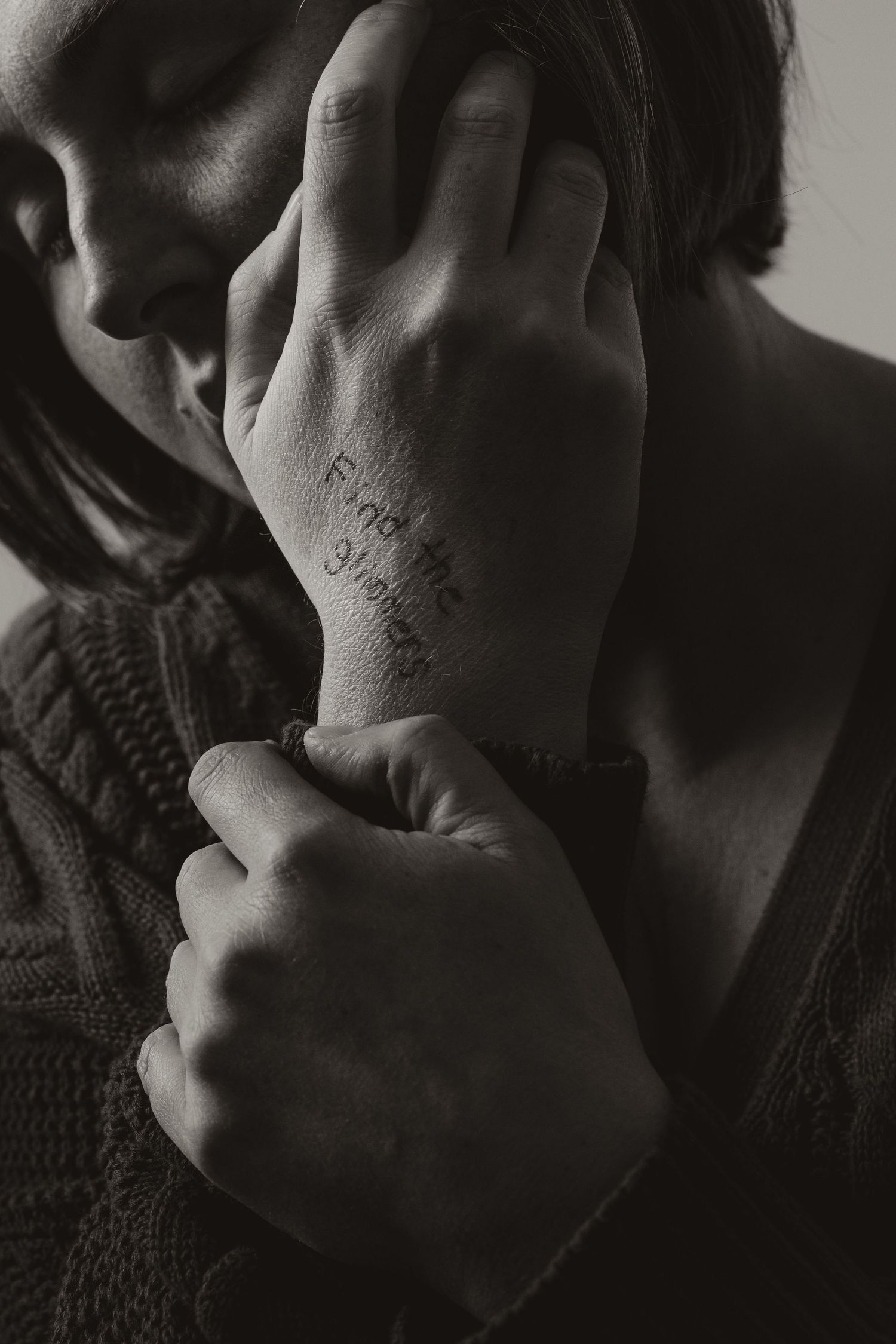 Black and white photograph of hands with words written on skin in moody dramatic lighting.