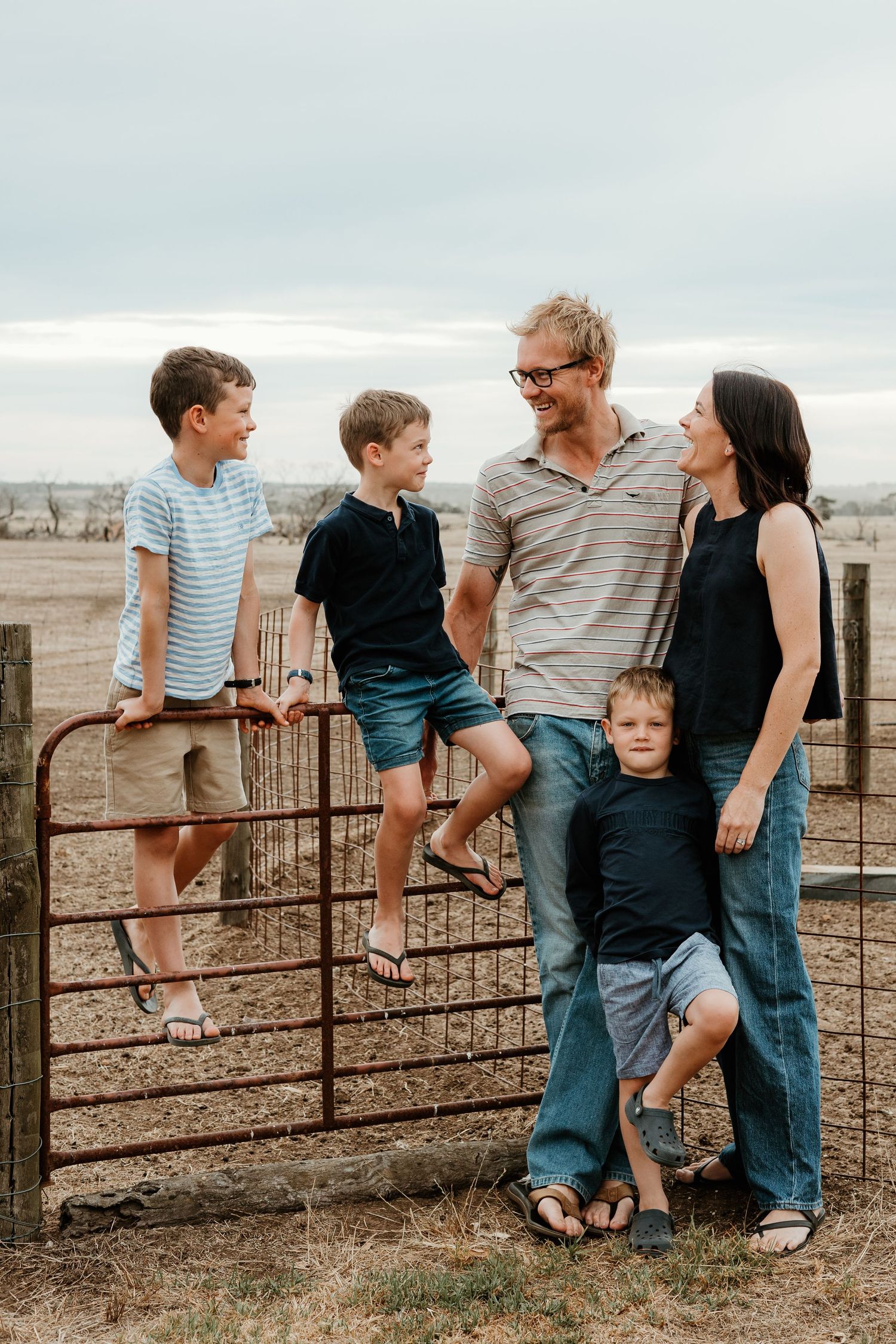 Family posing together on rustic metal gate in countryside setting.