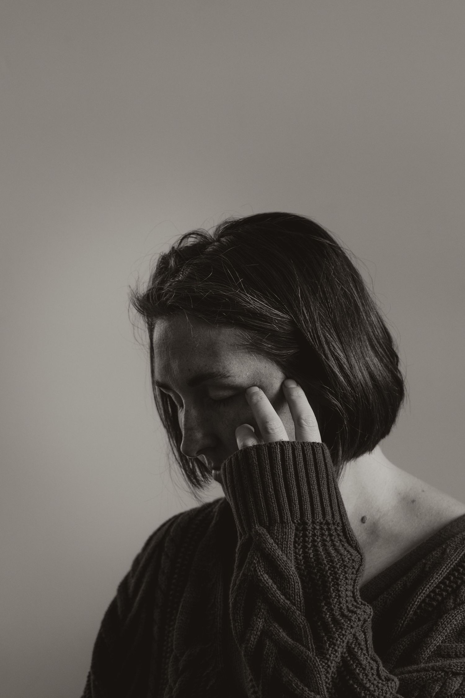 Black and white artistic portrait of someone in a knit sweater covering their face with one hand.