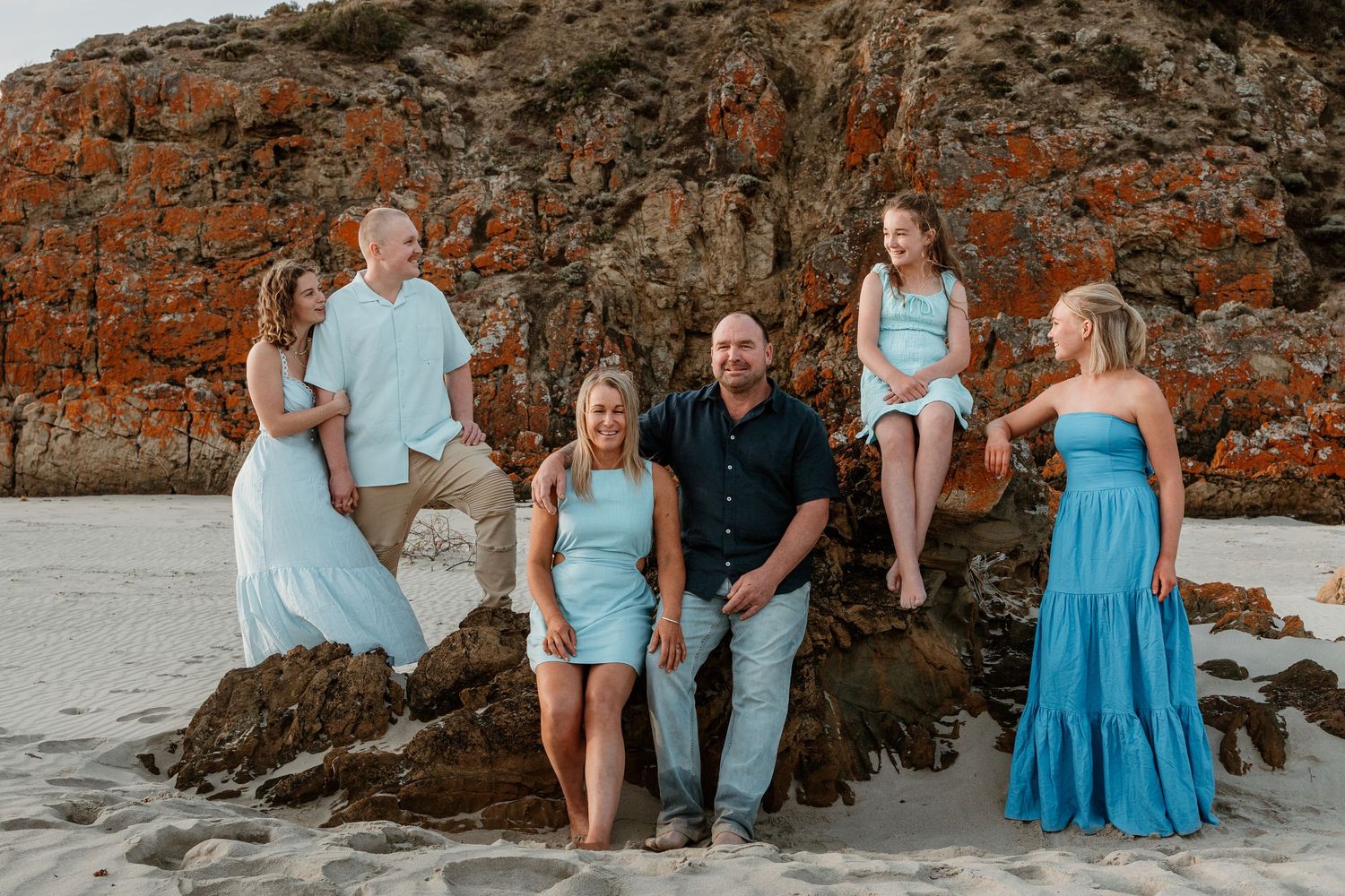Family group poses on rocky beach outcropping in coordinated blue and white outfits.