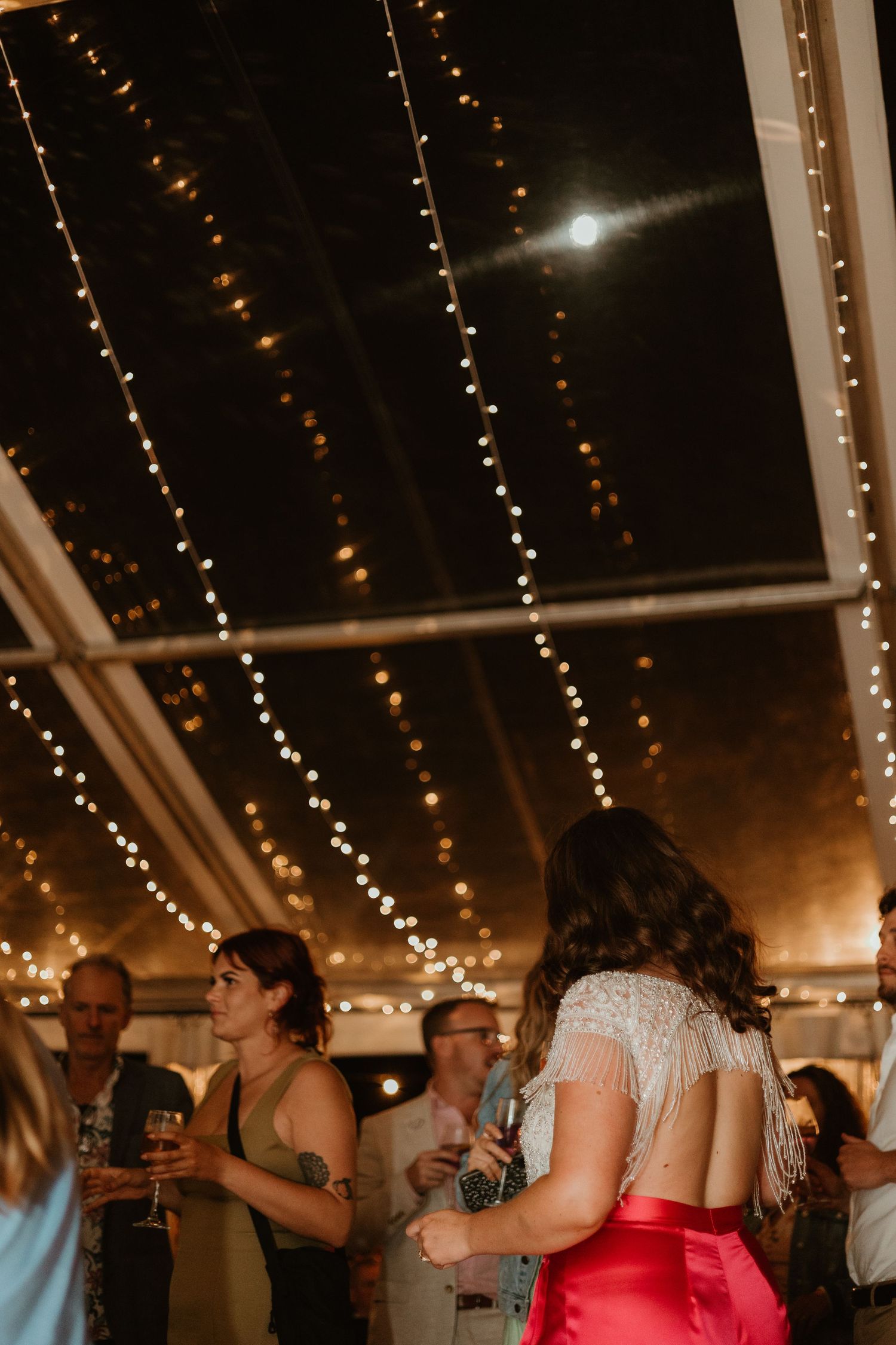 People dancing under warm string lights at a festive evening gathering.