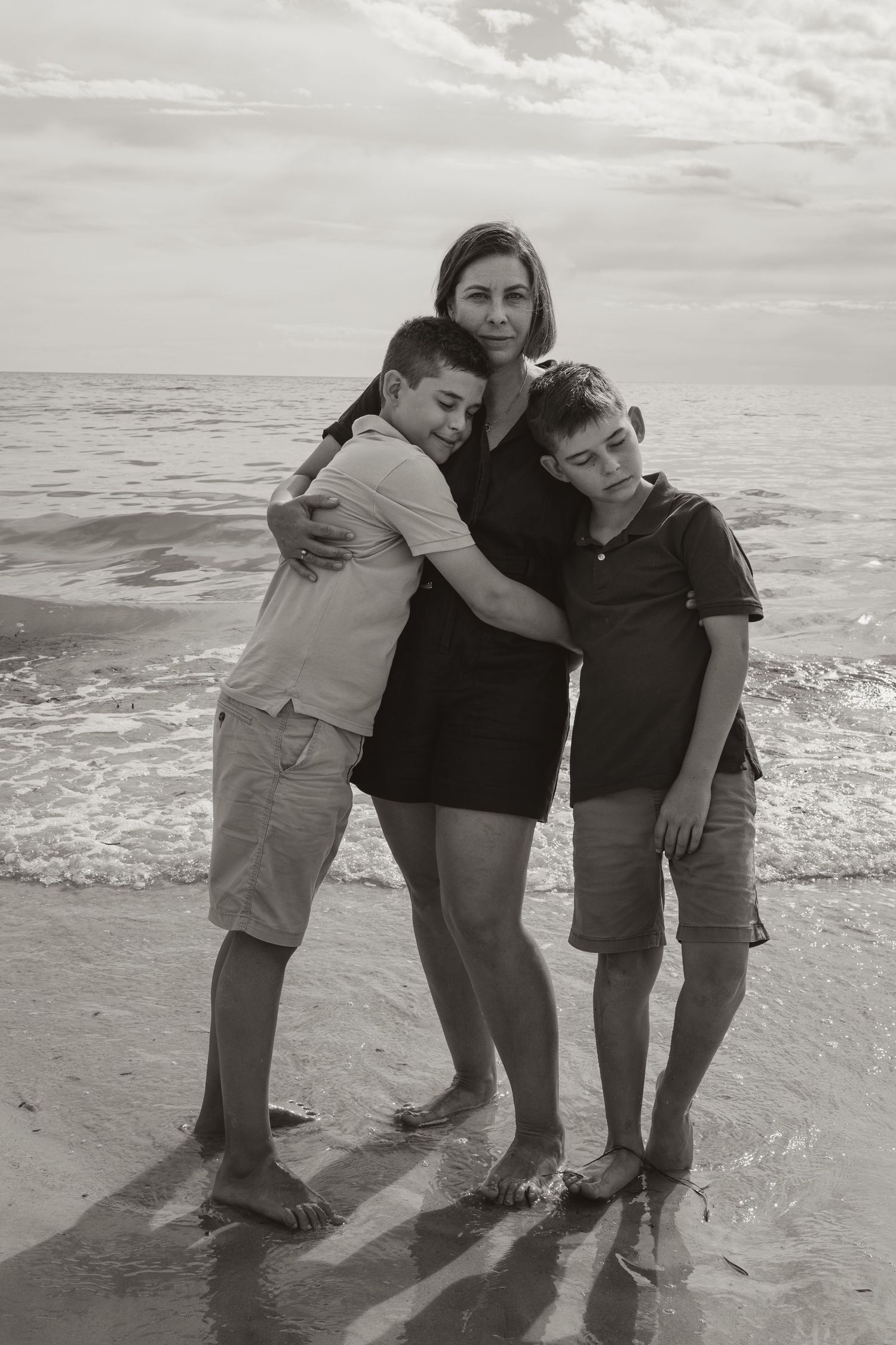 Family of three poses for casual beach portrait with ocean waves in background.