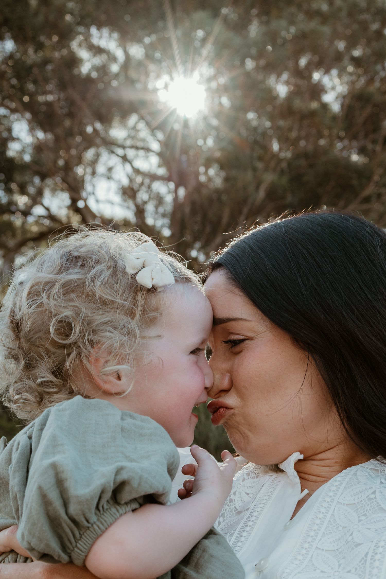 An intimate moment between parent and child captured in golden sunlight through trees.